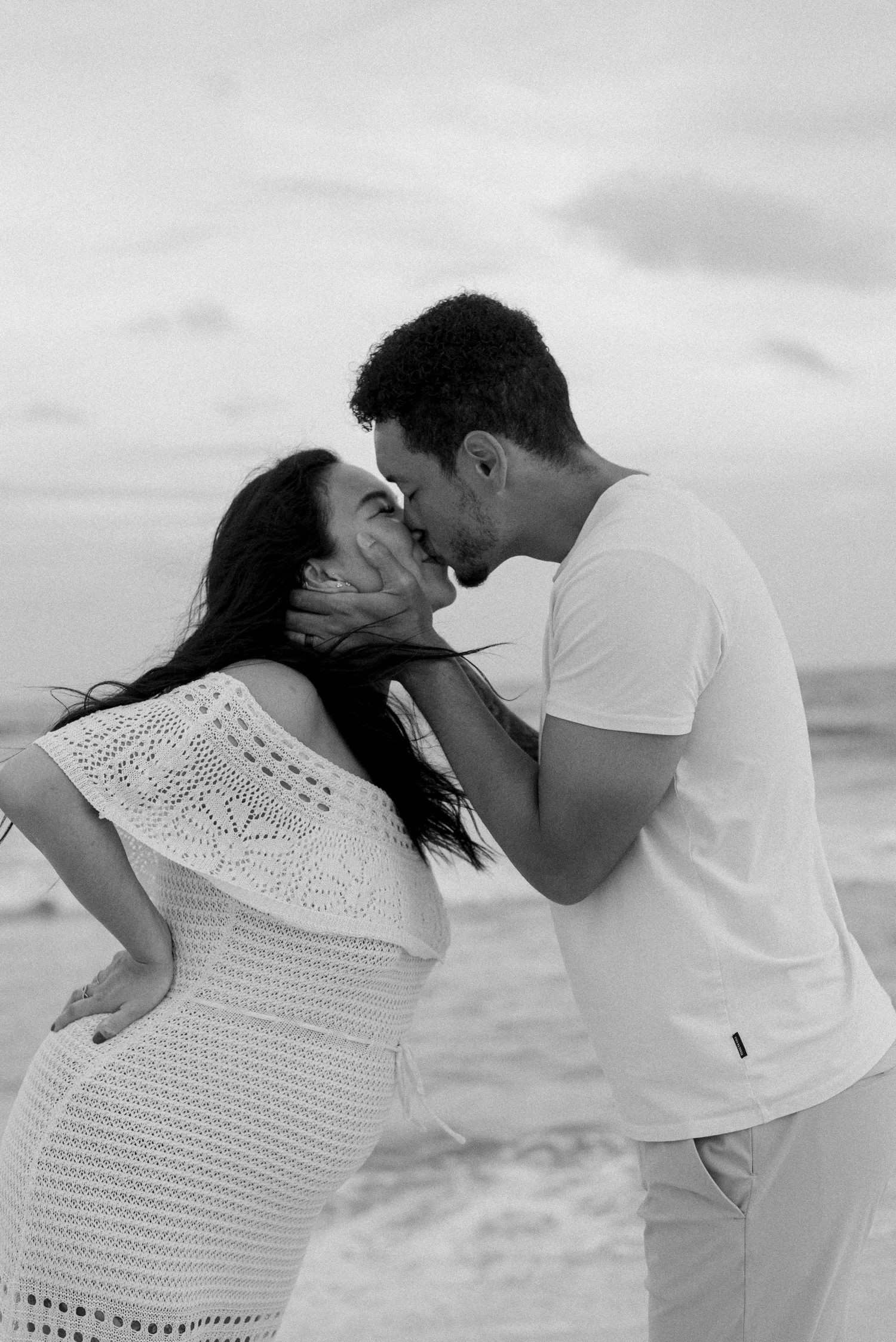 A romantic black and white photo sequence of a couple sharing tender moments on a beach in white outfits.