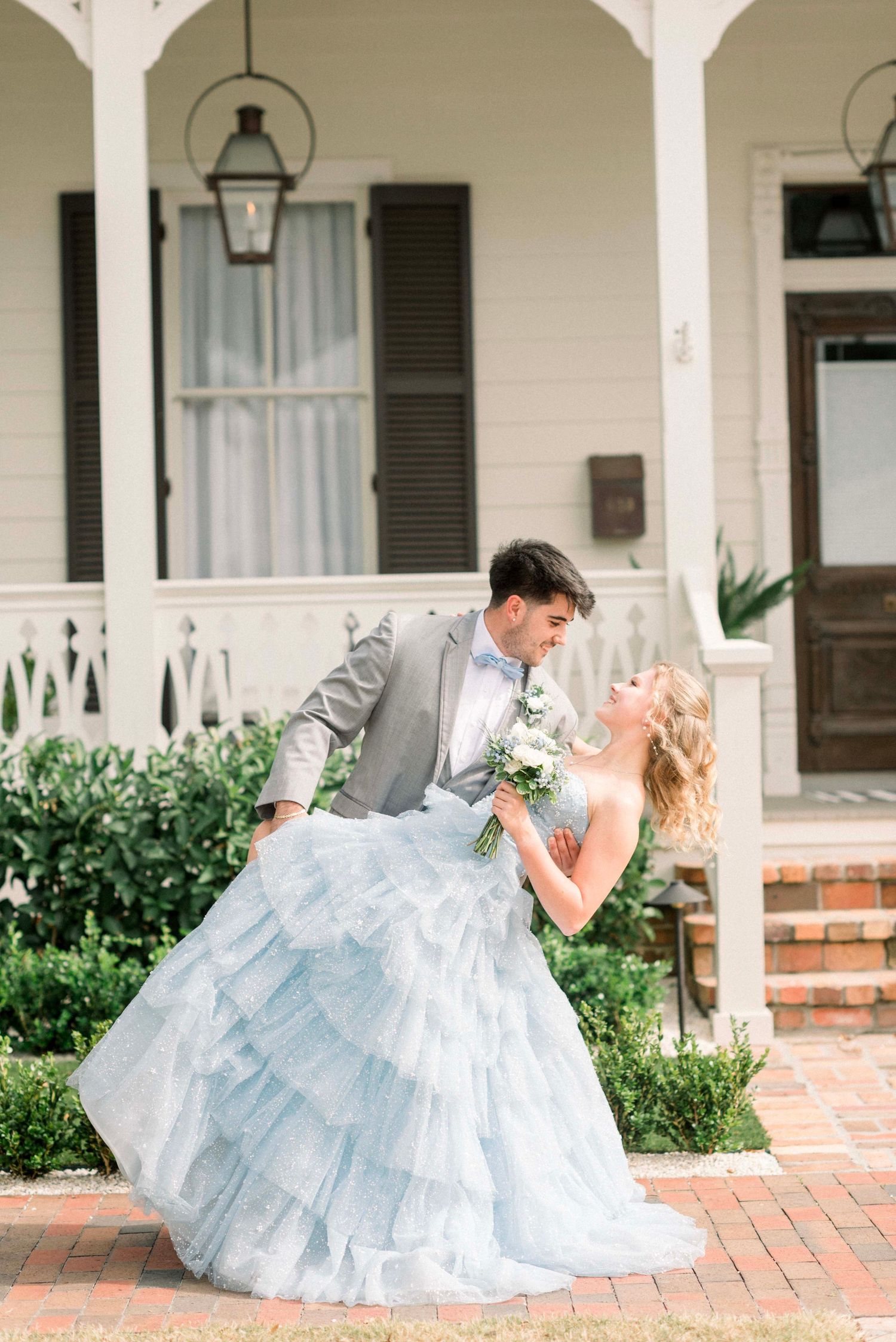 A couple in formal wear dances on a brick porch with white columns.
