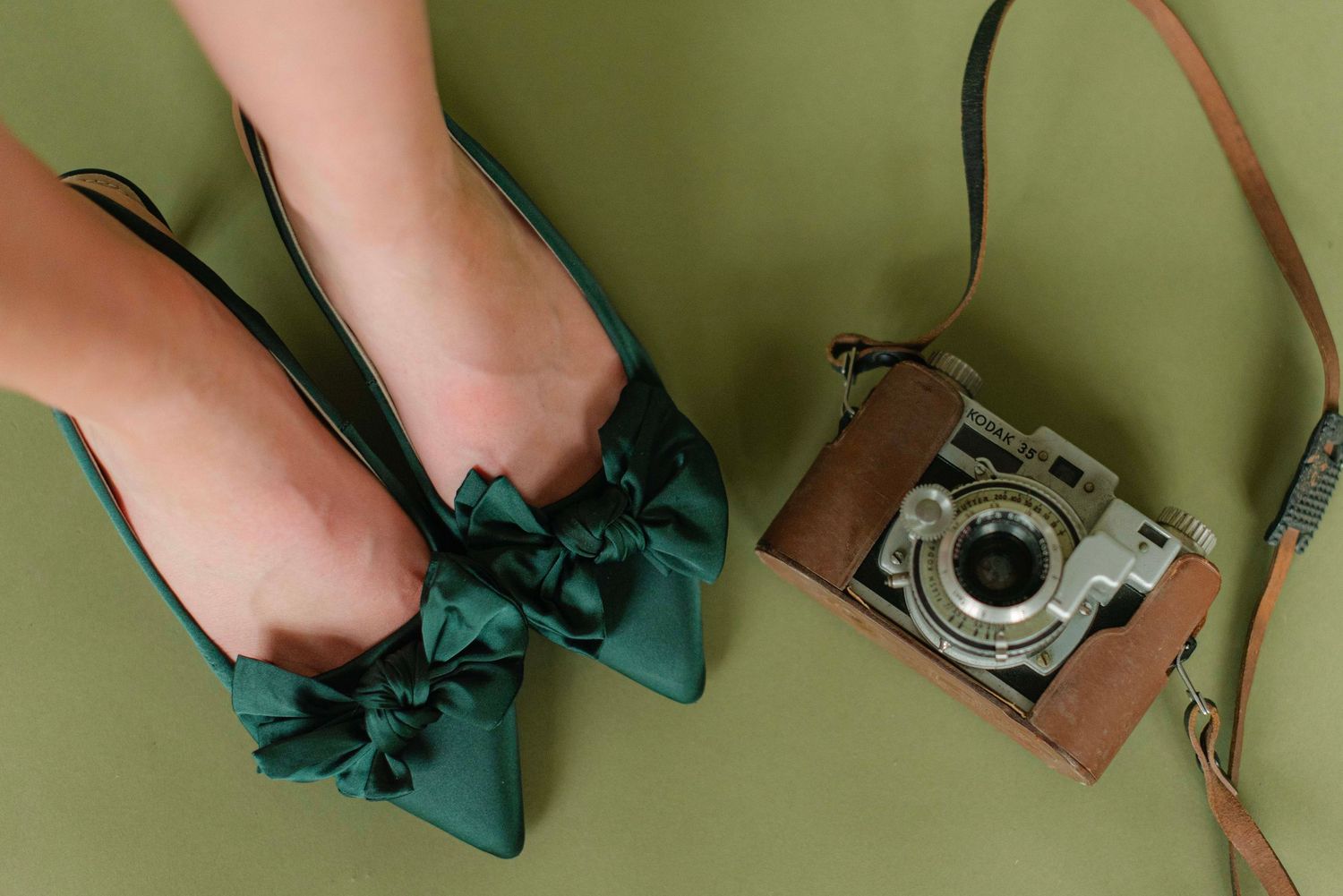 Close-up shots of legs wearing teal bow heels with a vintage camera against green backdrop.