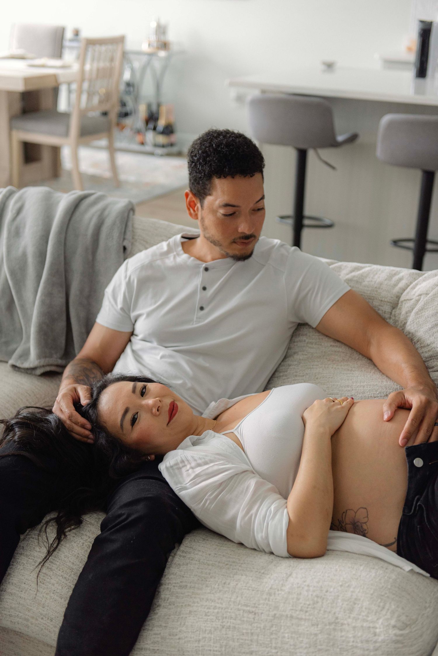 Expecting couple relaxes together on gray couch in modern living room.