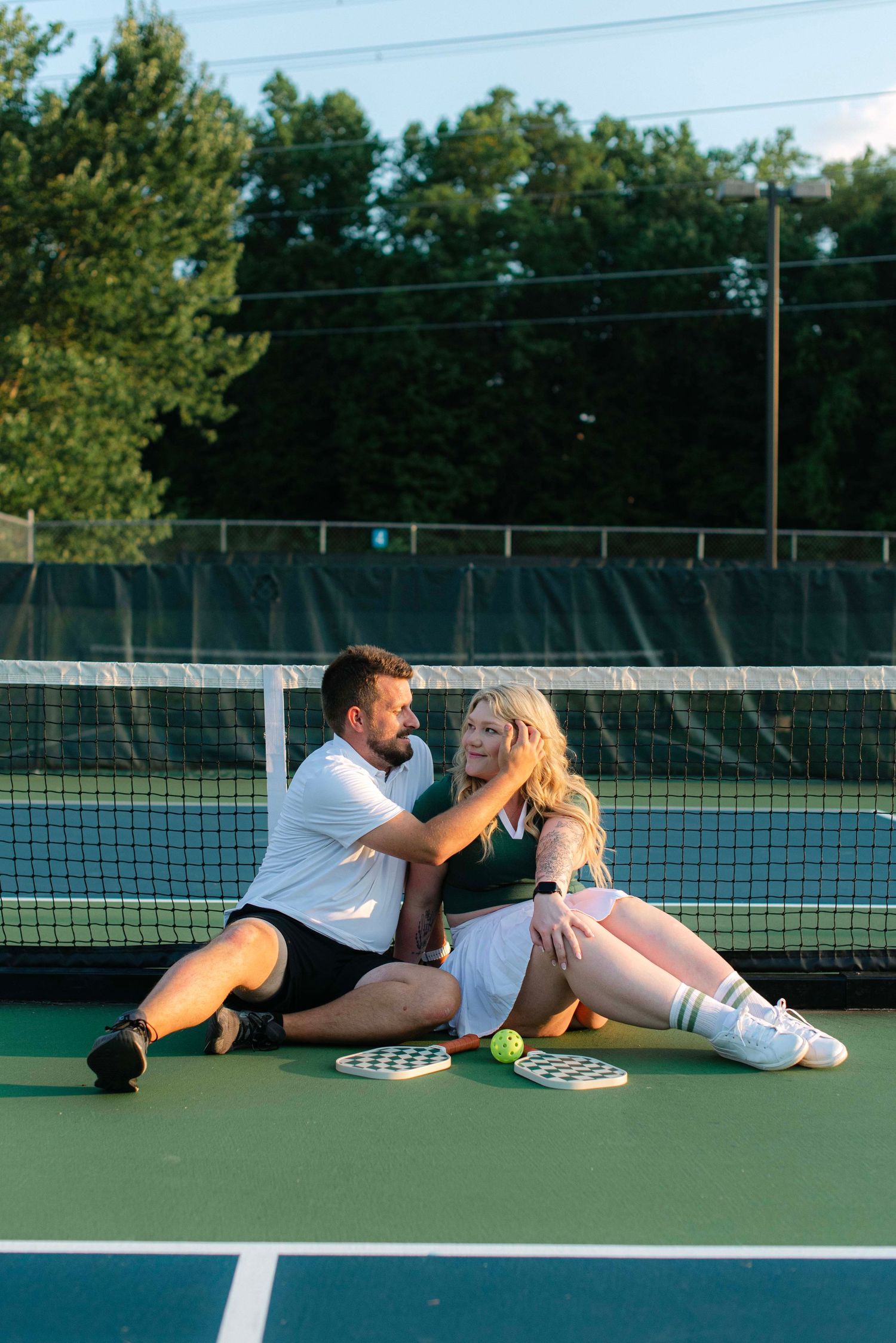 Two tennis players relax and share a playful moment while lying on a green tennis court.