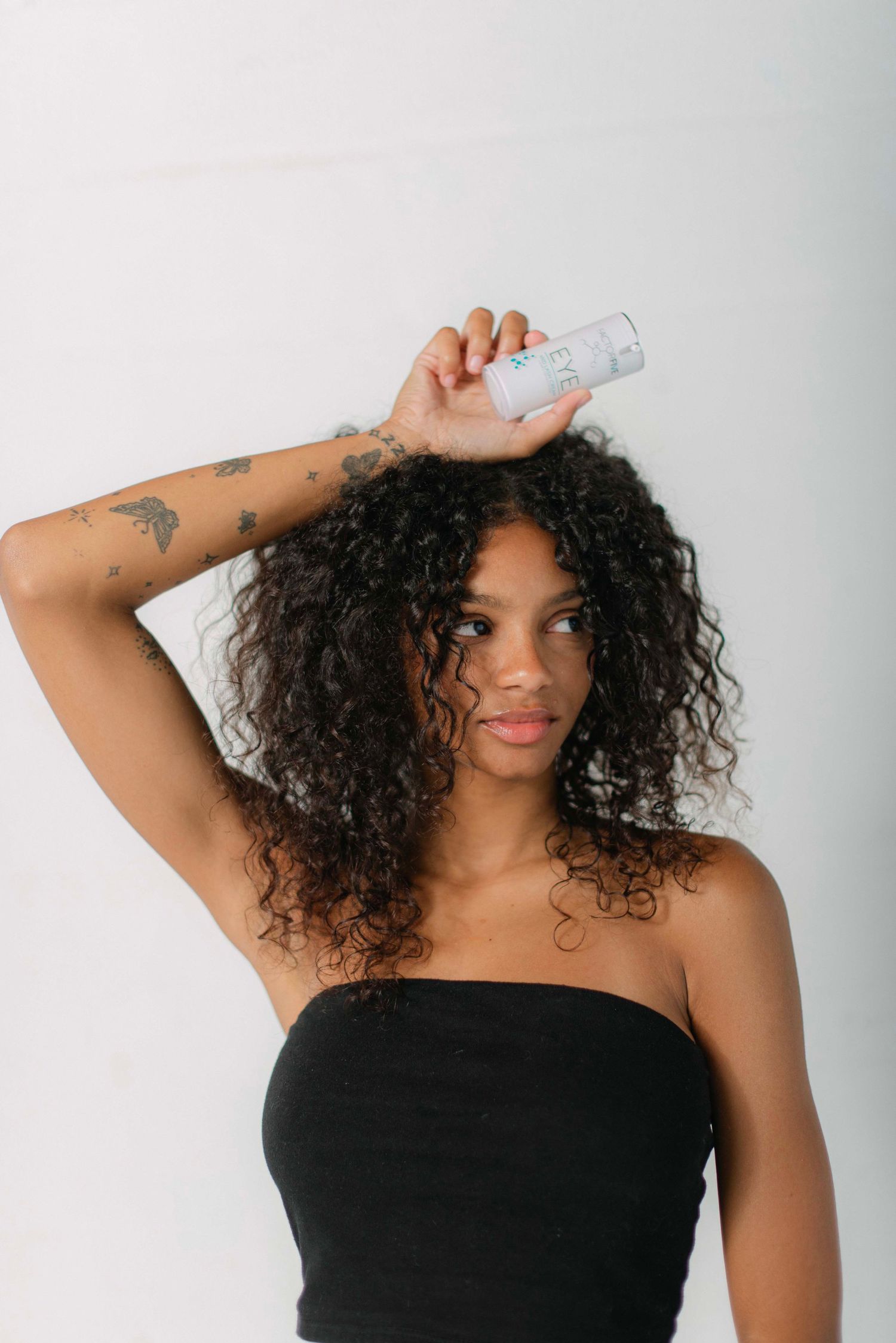 Person in black top styling curly hair against white studio background.