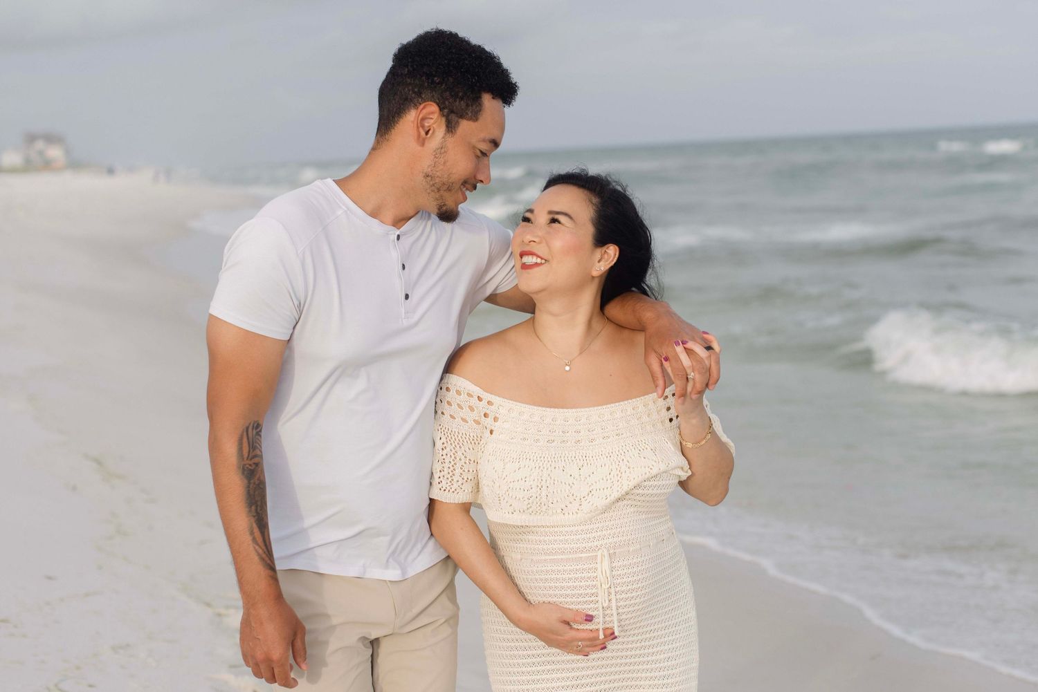 A couple shares tender moments on a sandy beach with waves crashing behind them during a romantic photoshoot.