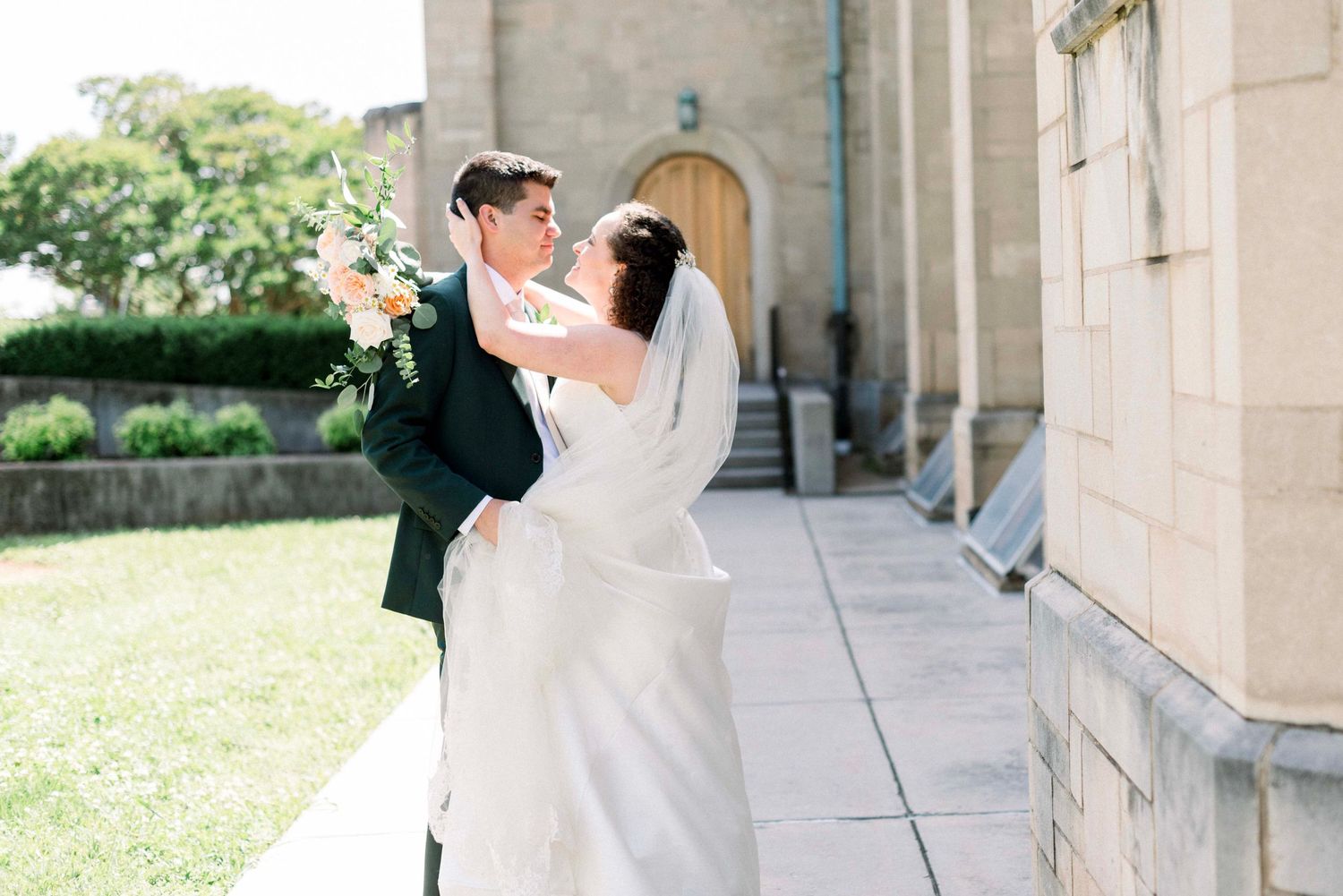 A joyful bride and groom dance and celebrate together on a sunny patio with stone columns.