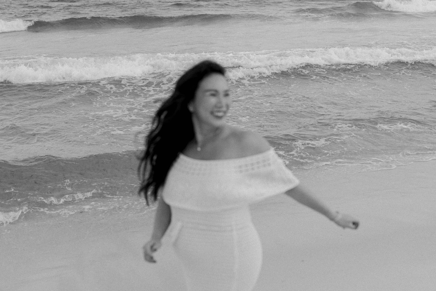 Two people dancing playfully along the shoreline with waves crashing in the background.