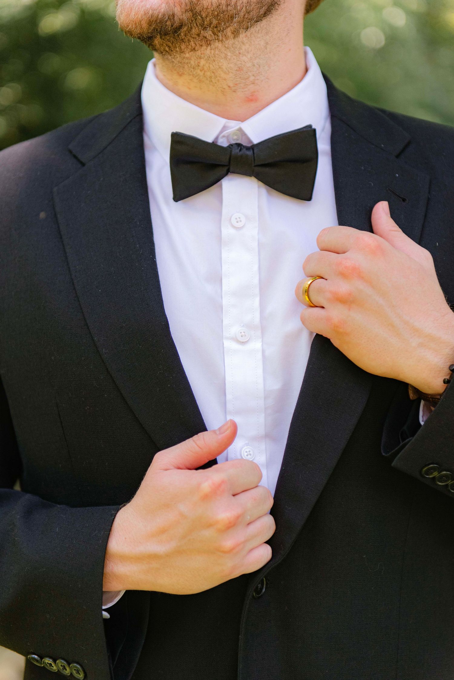 Close-up details of a groom adjusting his black bow tie and tuxedo.