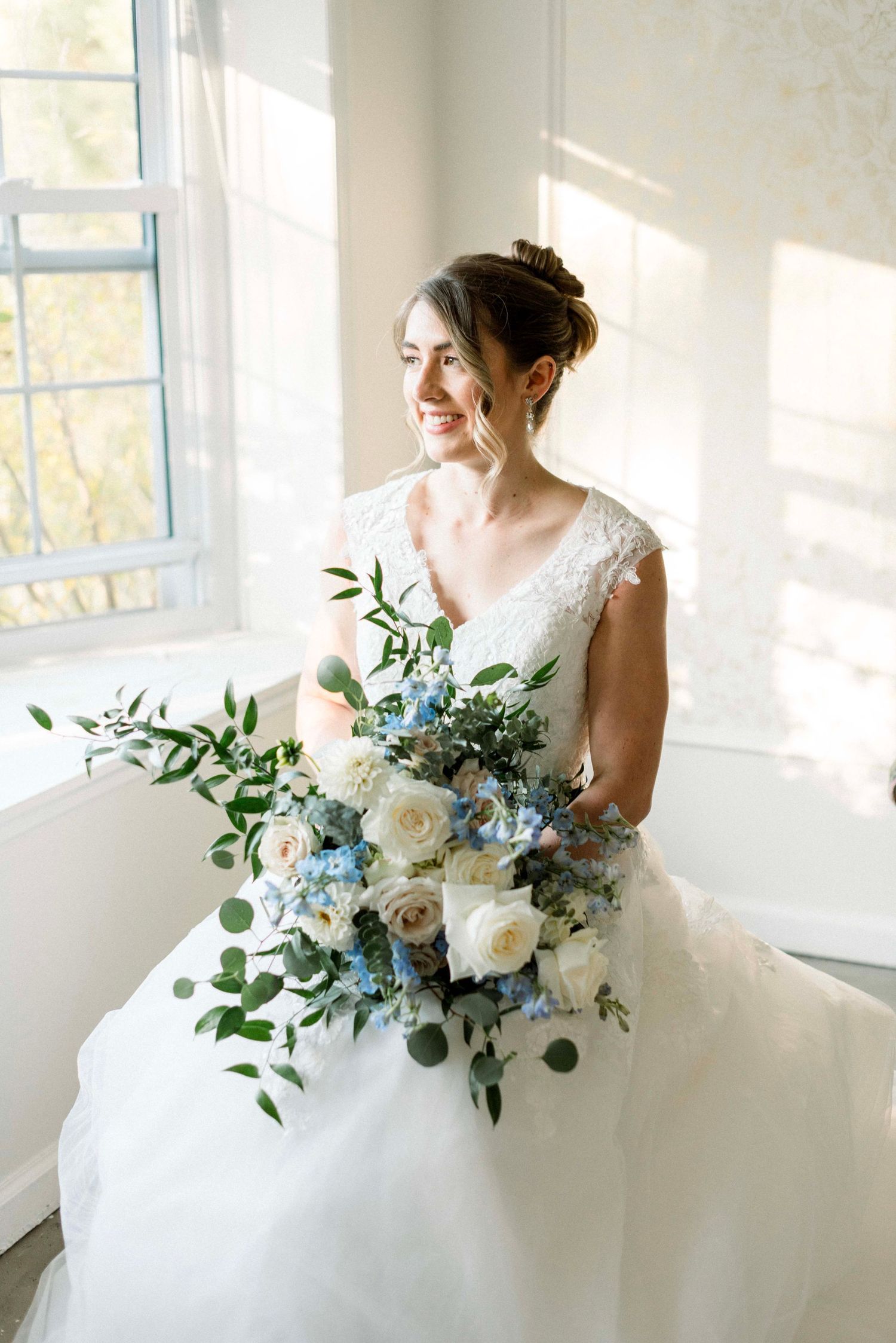 An elegant bridal portrait featuring a white gown and blue and white floral bouquet.