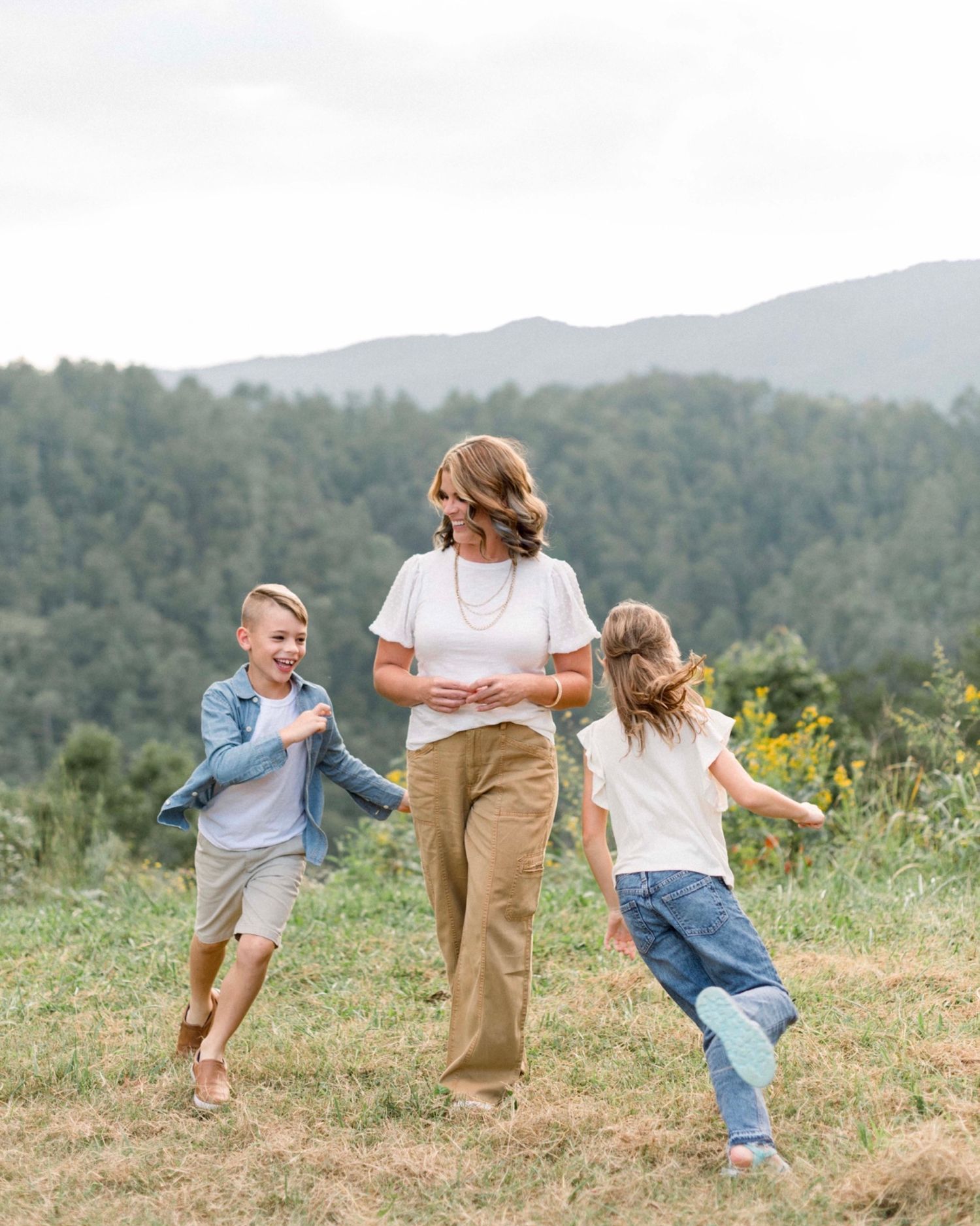 A playful sequence of movement captures children dancing and twirling on a grassy hillside against the smoky mountain backdrop with mom