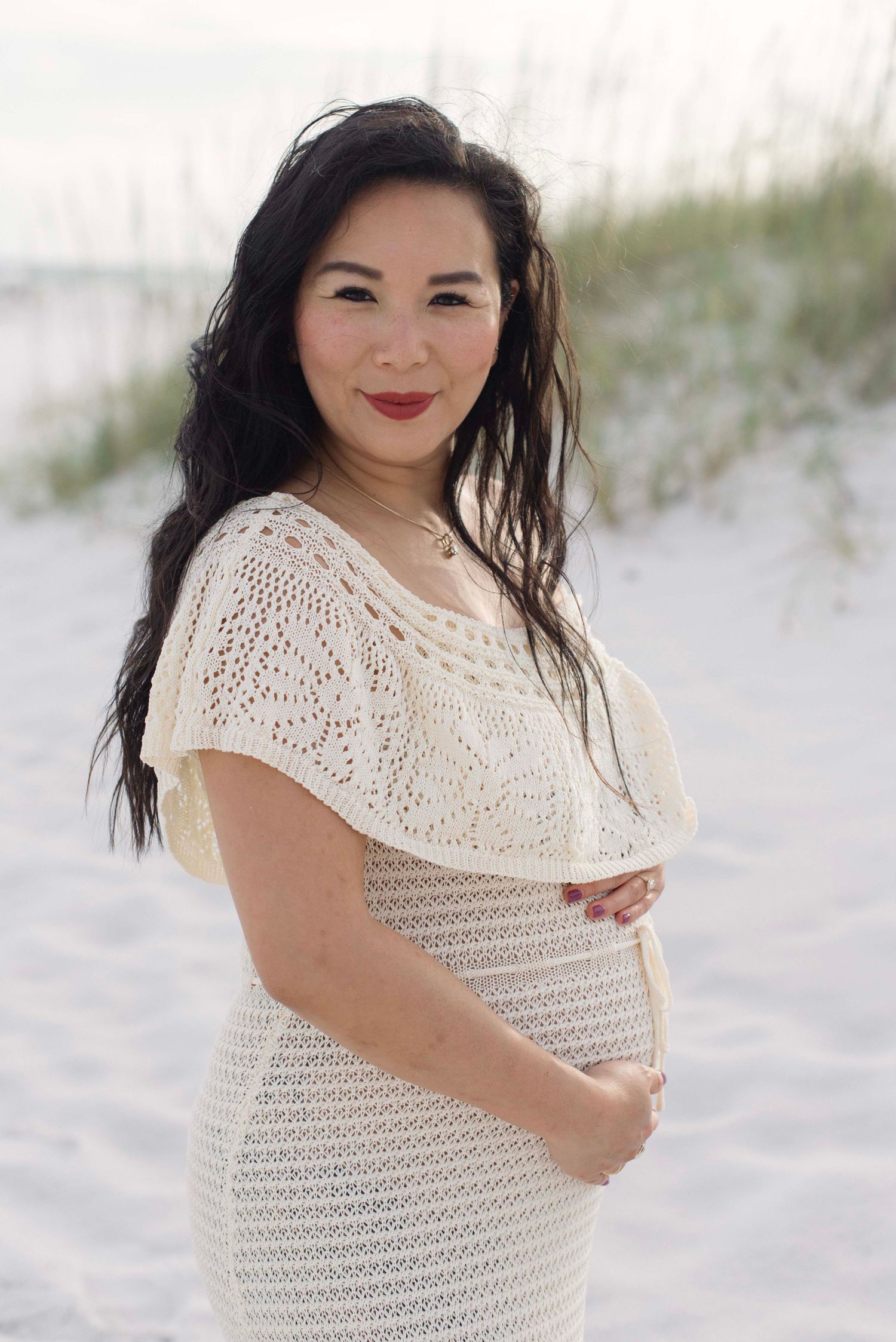 A series of maternity photos on a white sandy beach featuring a woman in a cream crochet dress.