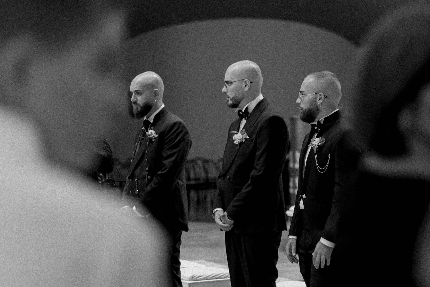 A group of bald men in black suits stand together in a formal setting.