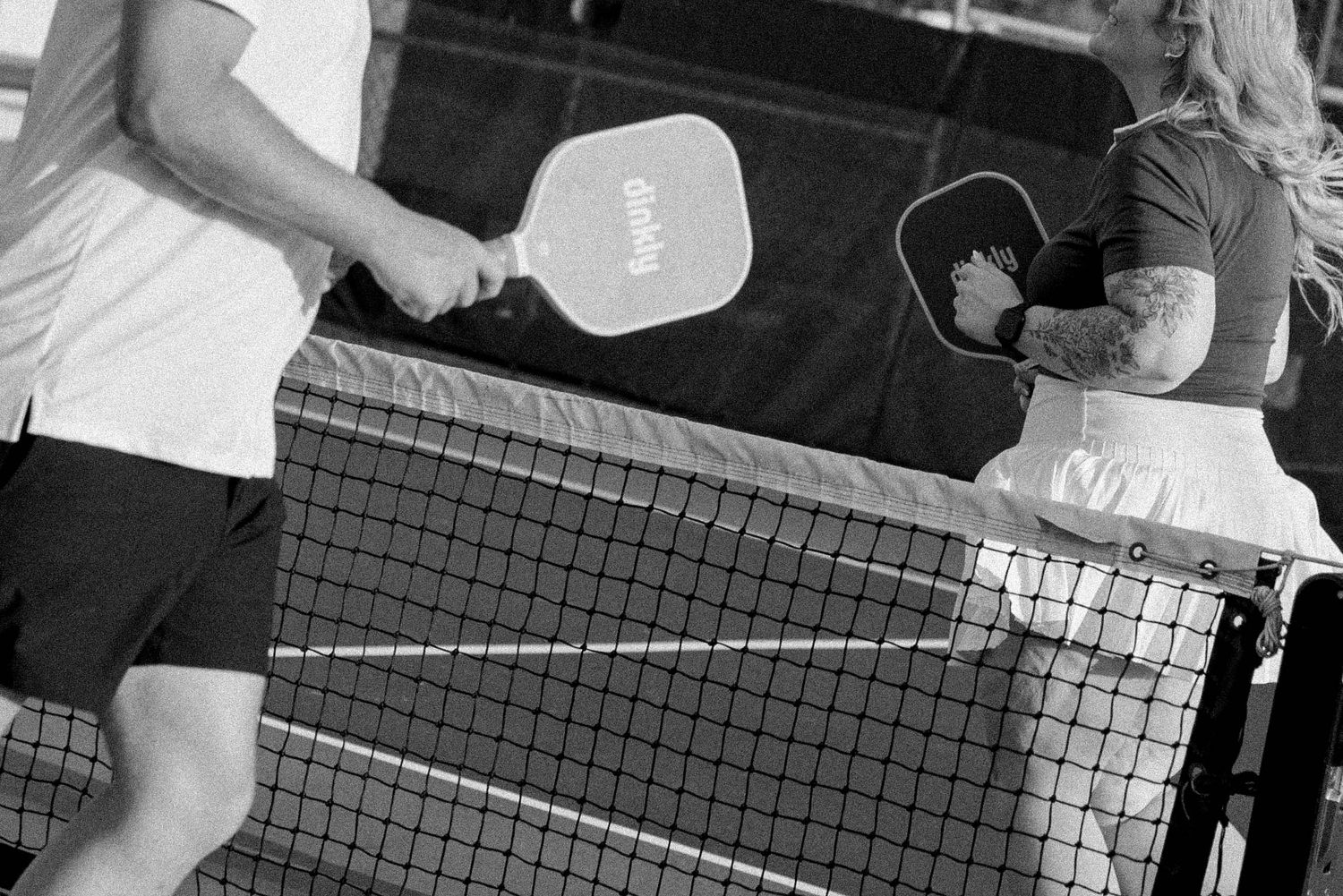 Black and white photo of a tennis match in progress with players positioned at the net during play.