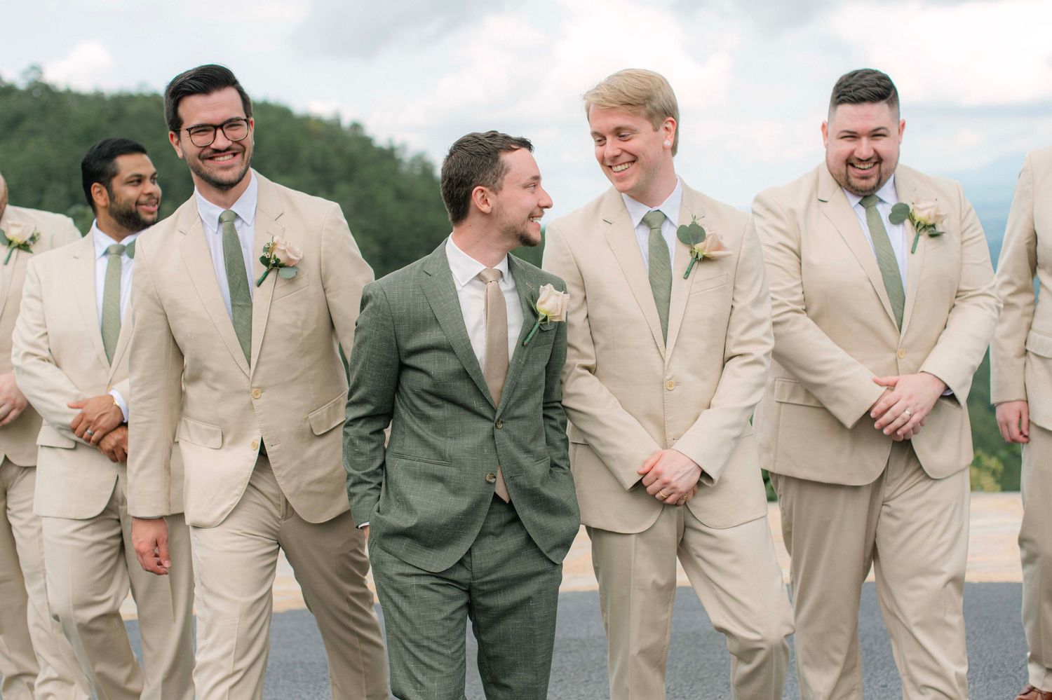 Groomsmen in light beige suits and one in sage green pose together outdoors.