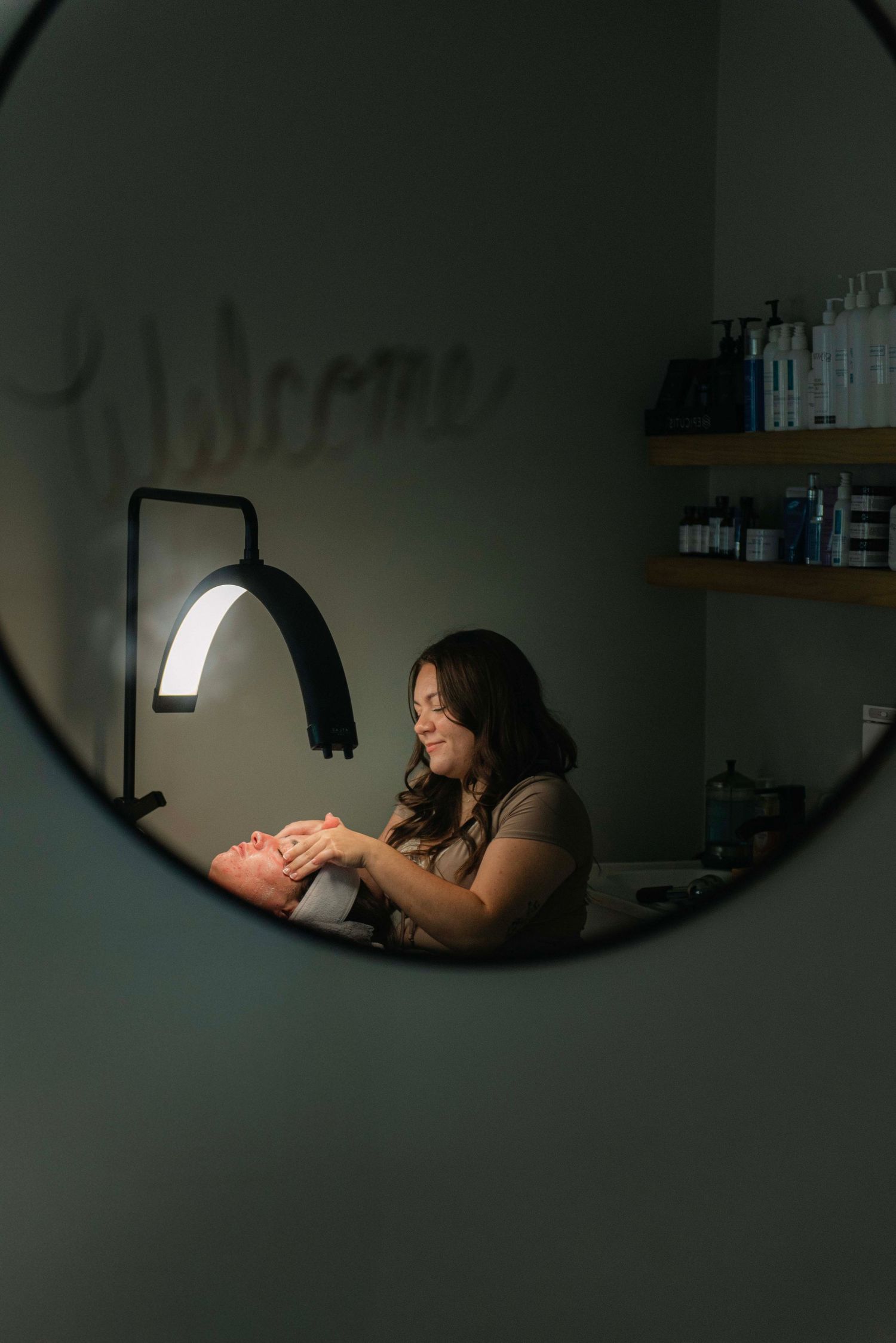 Dark reflection in oval mirror showing spa treatment room interior.