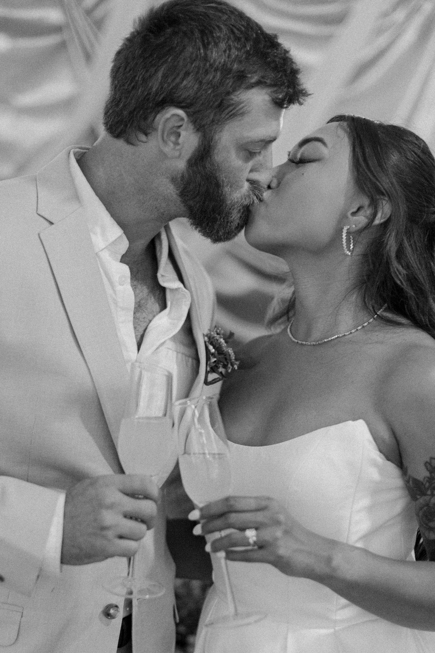 A romantic black and white wedding photo captures a tender kiss between newlyweds in matching white attire.