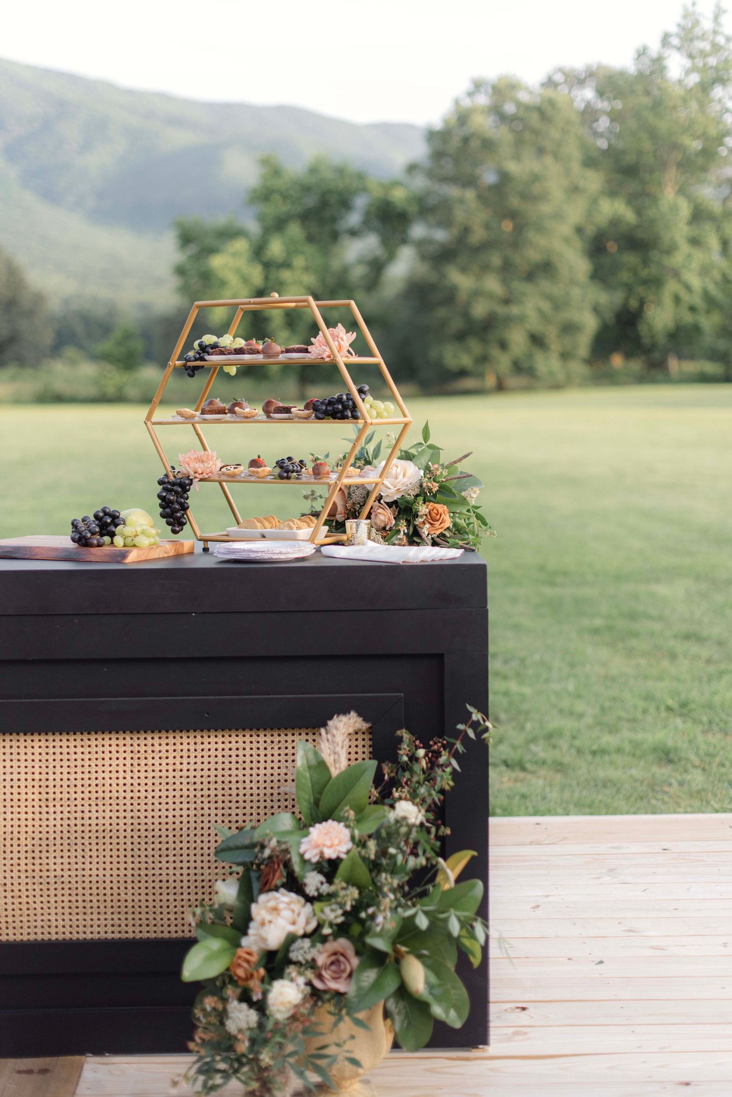 Modern black tables with rattan accents decorated with copper geometric frames and floral arrangements in an outdoor setting.
