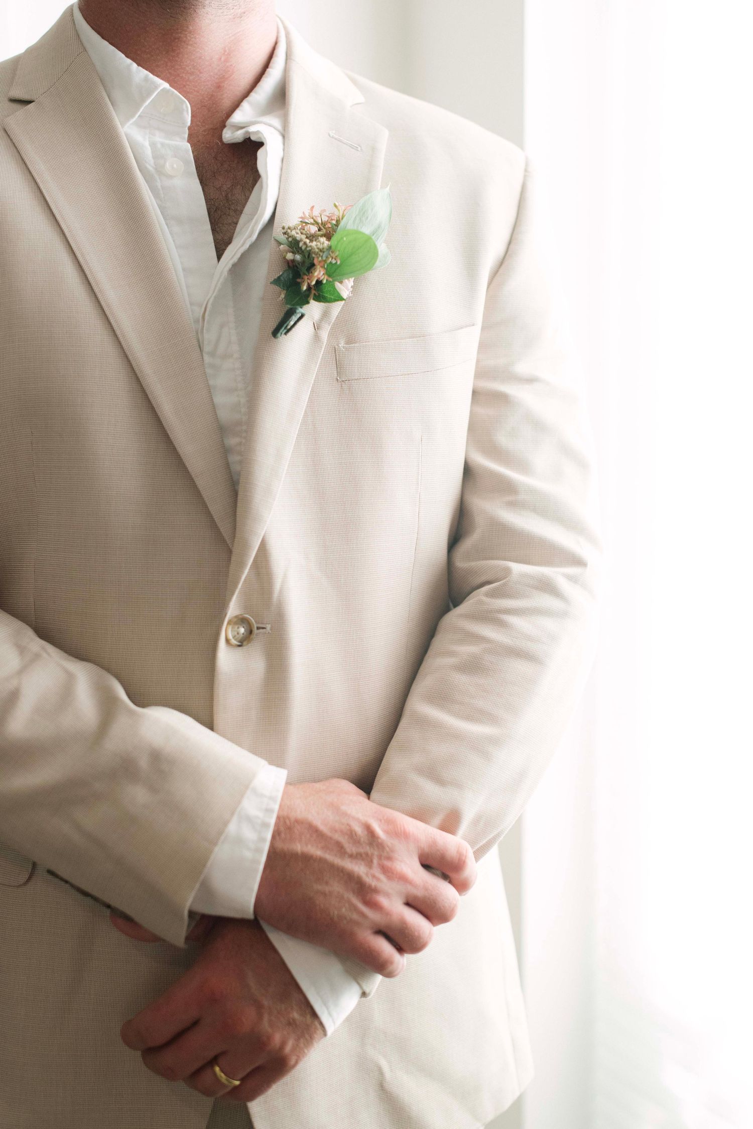 A row of groomsmen wearing cream colored suits with small green boutonnieres stand together at a formal event.