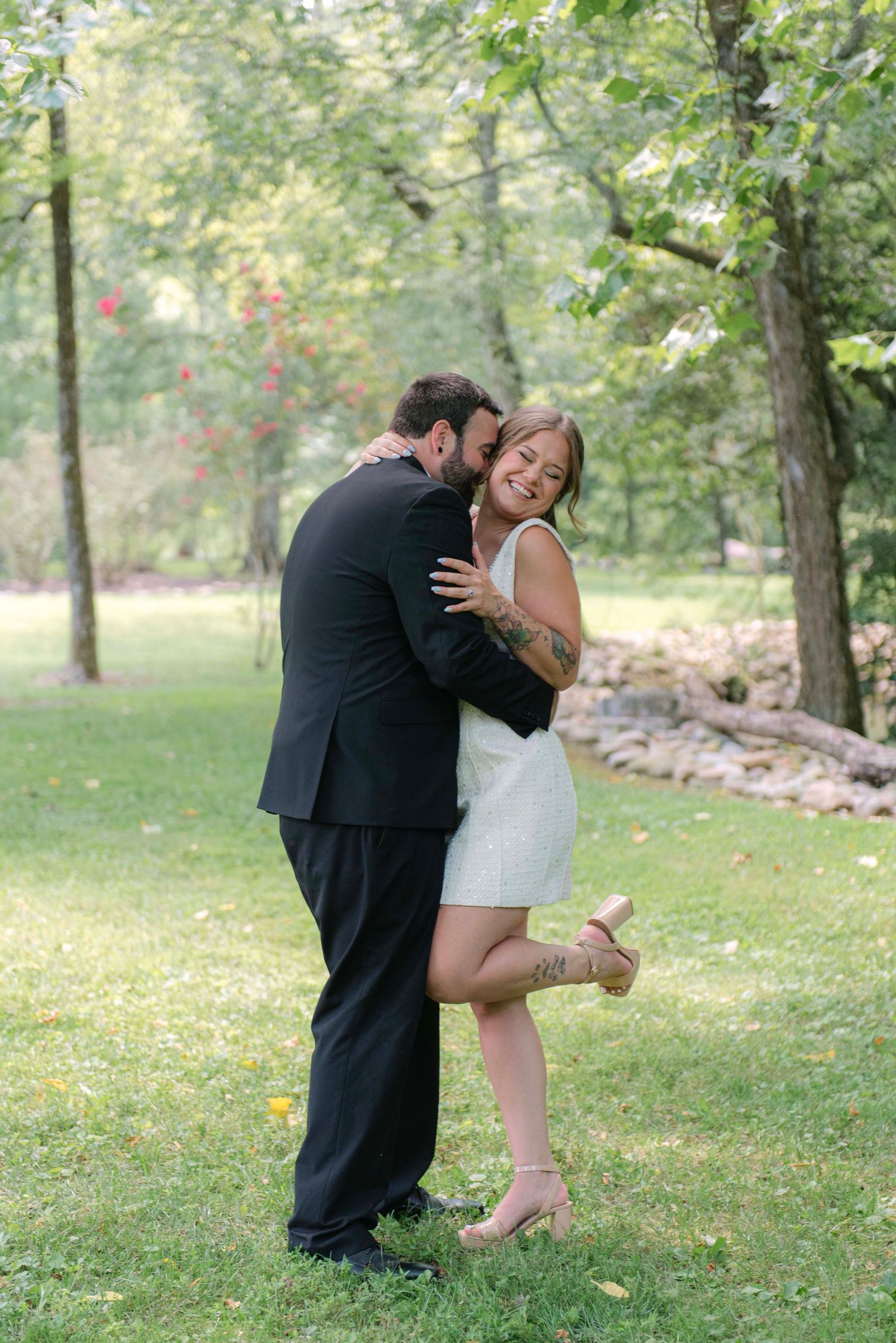 A romantic couple shares a tender moment in a sunlit garden setting wearing formal attire.