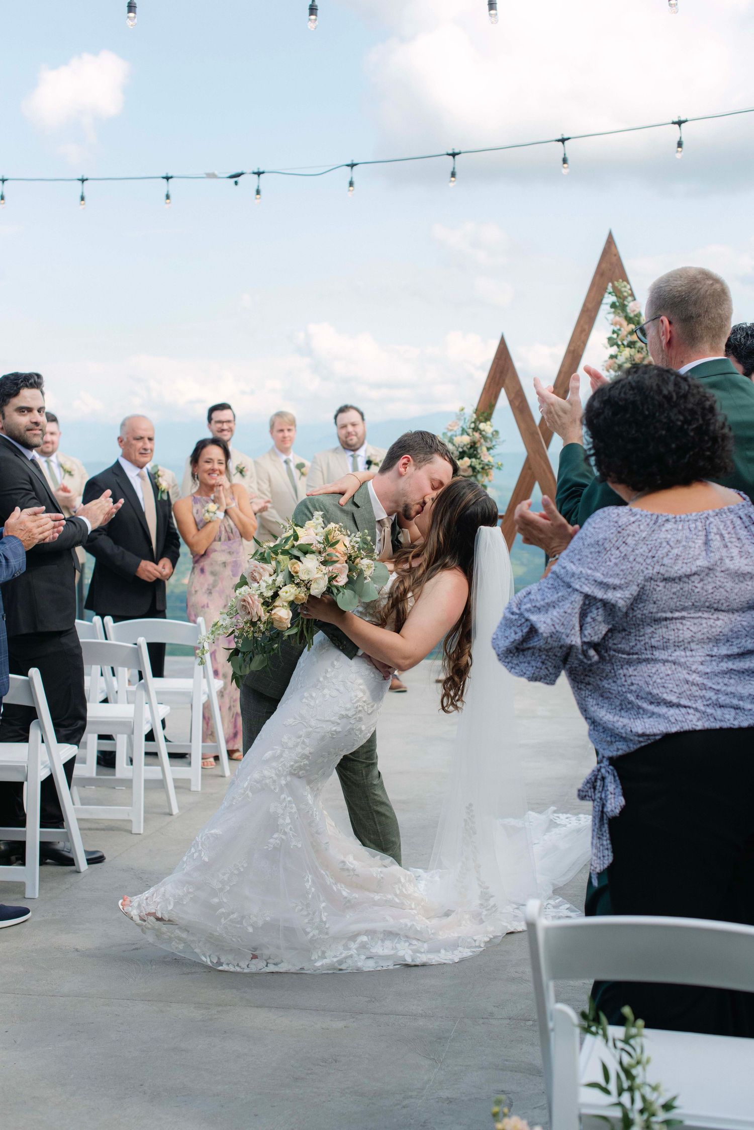 Wedding guests celebrate on an outdoor terrace with string lights and mountain views.