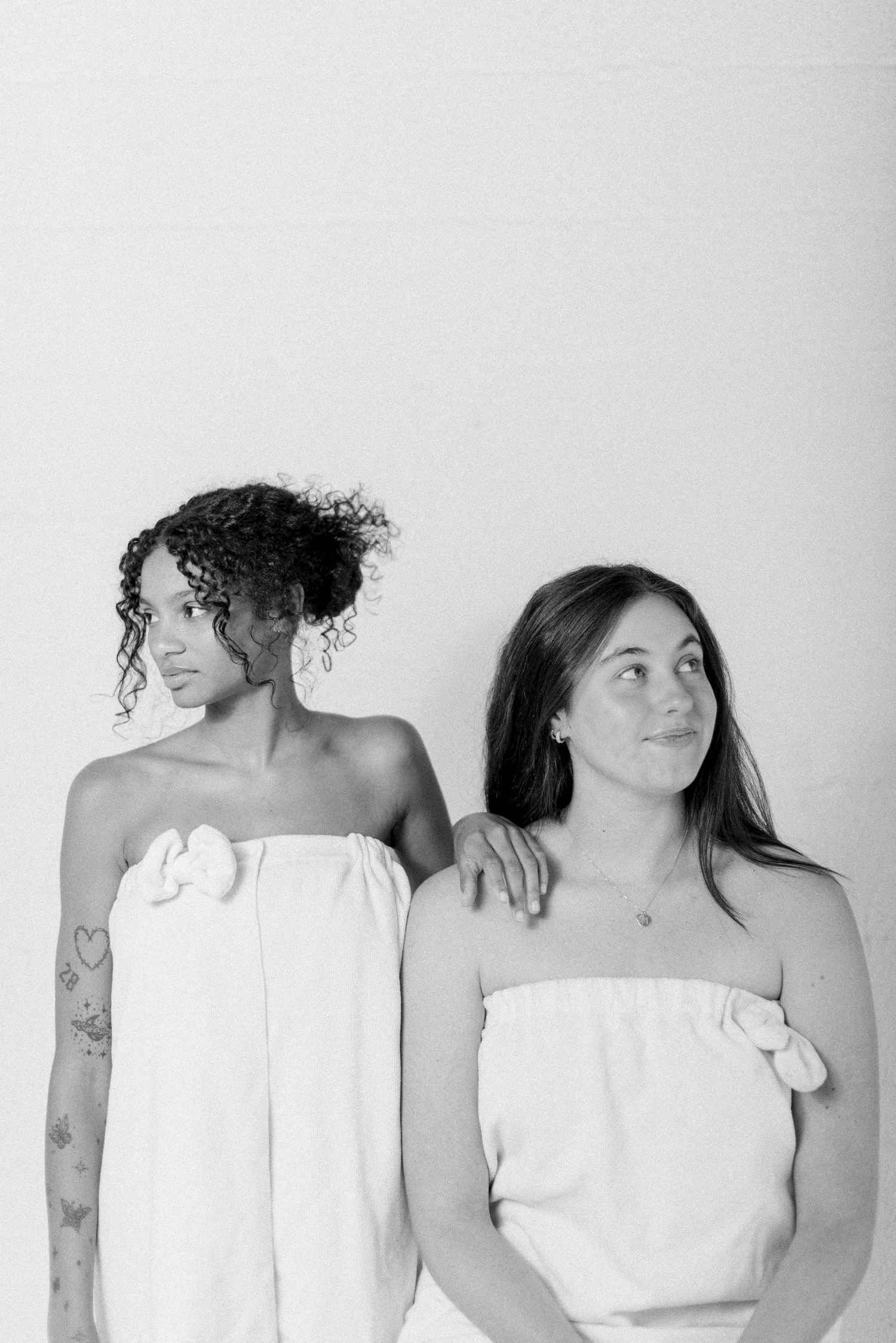 Models in white strapless tops posing together against white background.