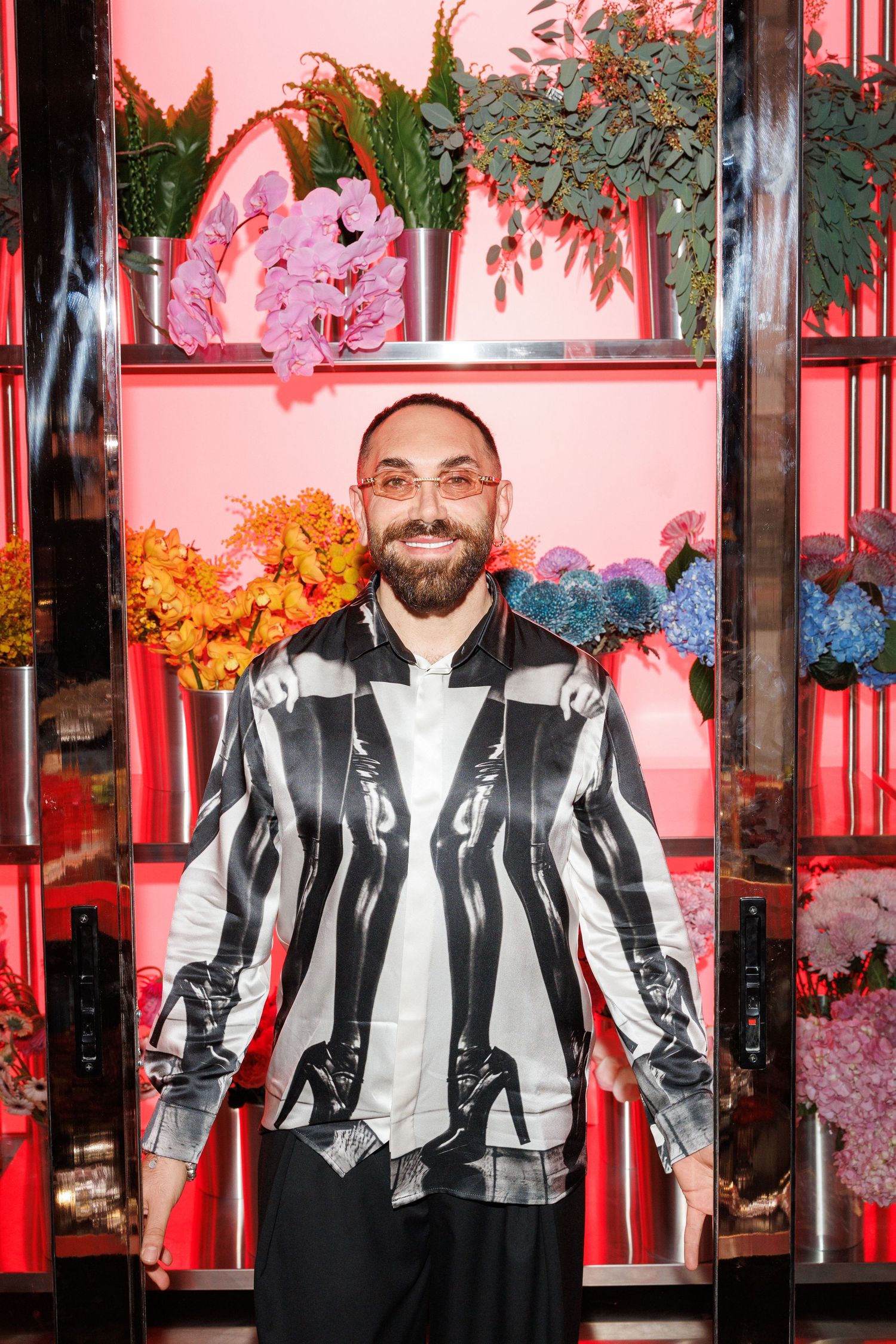 Person wearing black and white striped jacket poses against pink backdrop with decorative greenery and lighting.