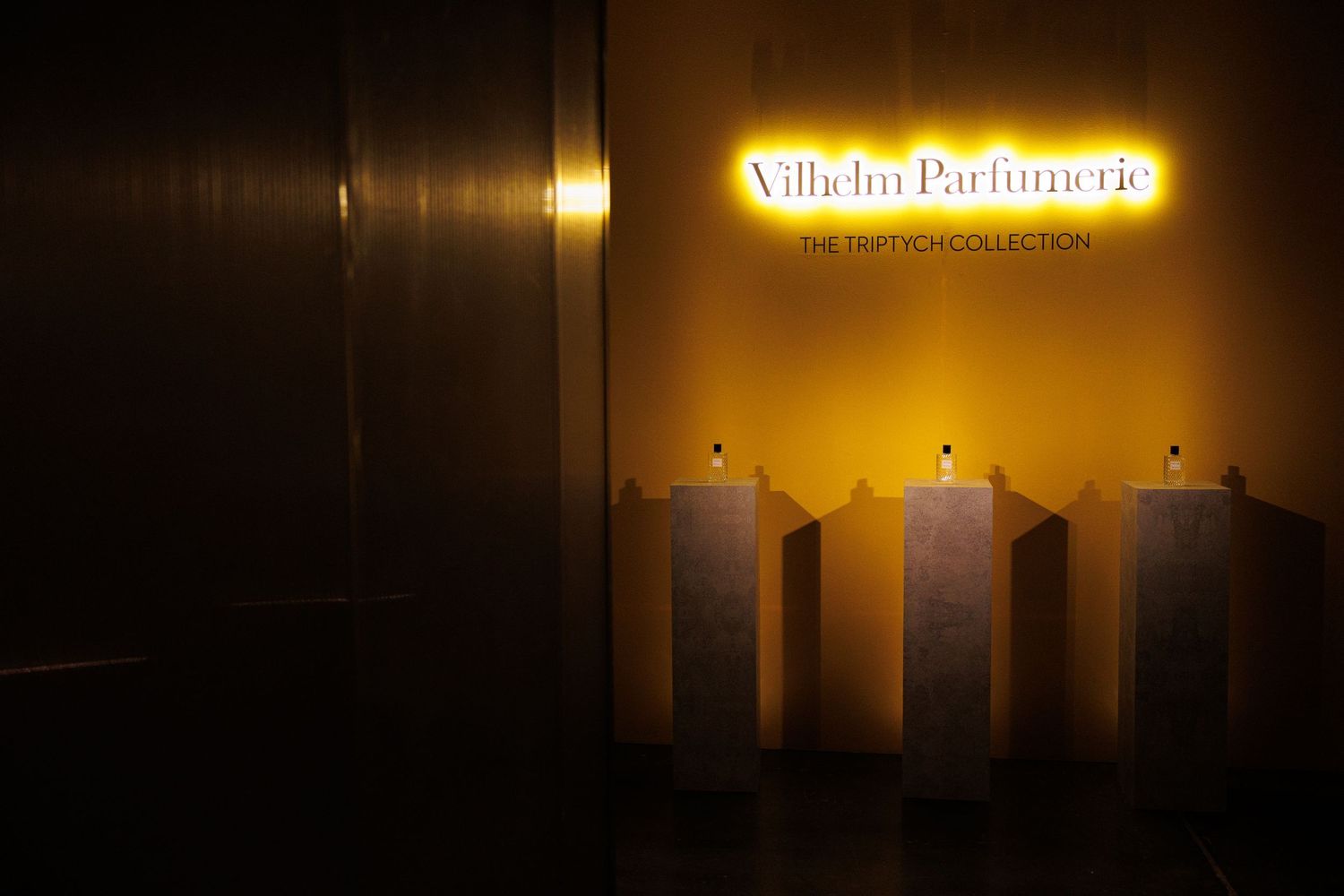 Illuminated 'Vilhelm Parfumerie' sign glowing in warm light against dark background.
