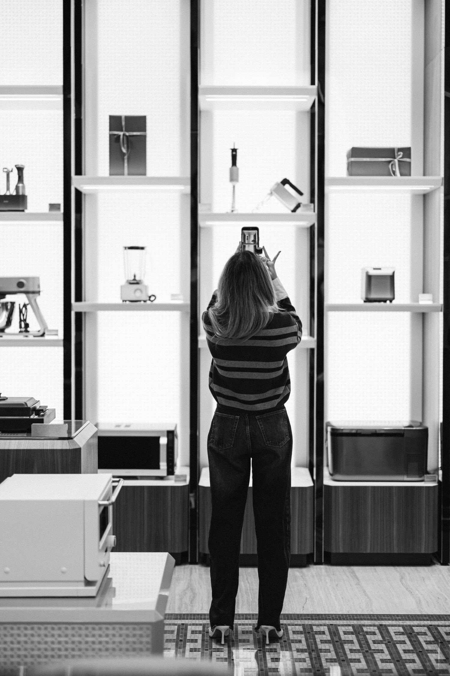 Black and white photo of illuminated retail display cases with shelving units along a wall.