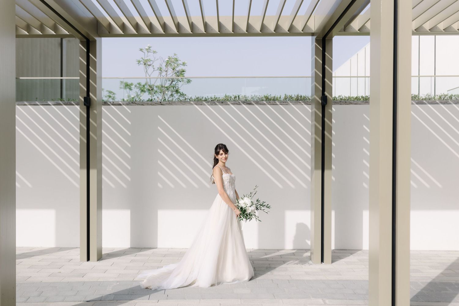 Modern wedding venue with white pergola and natural lighting creating dramatic shadows.