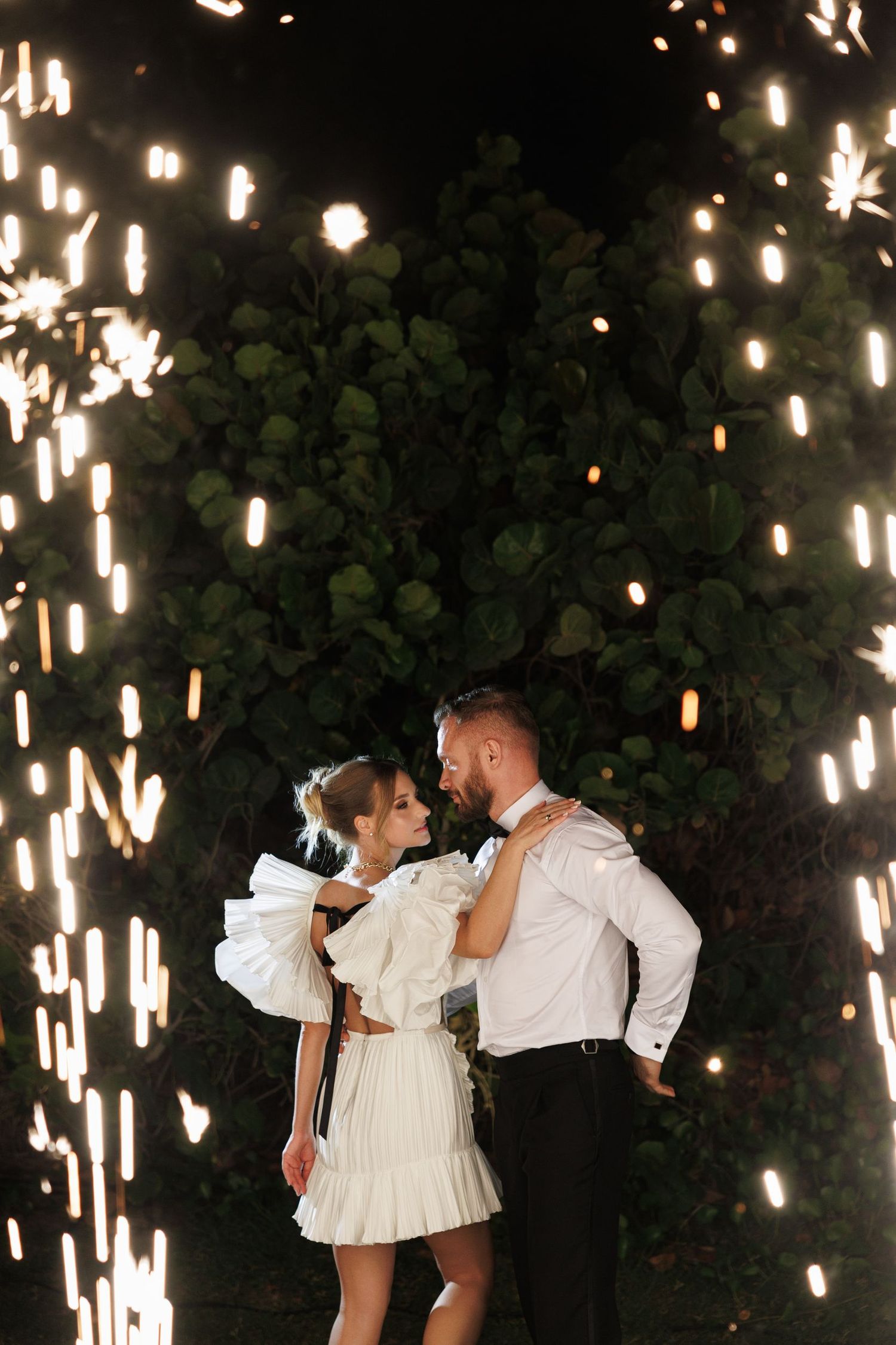 A romantic couple dancing under a magical display of hanging lights in a garden setting.