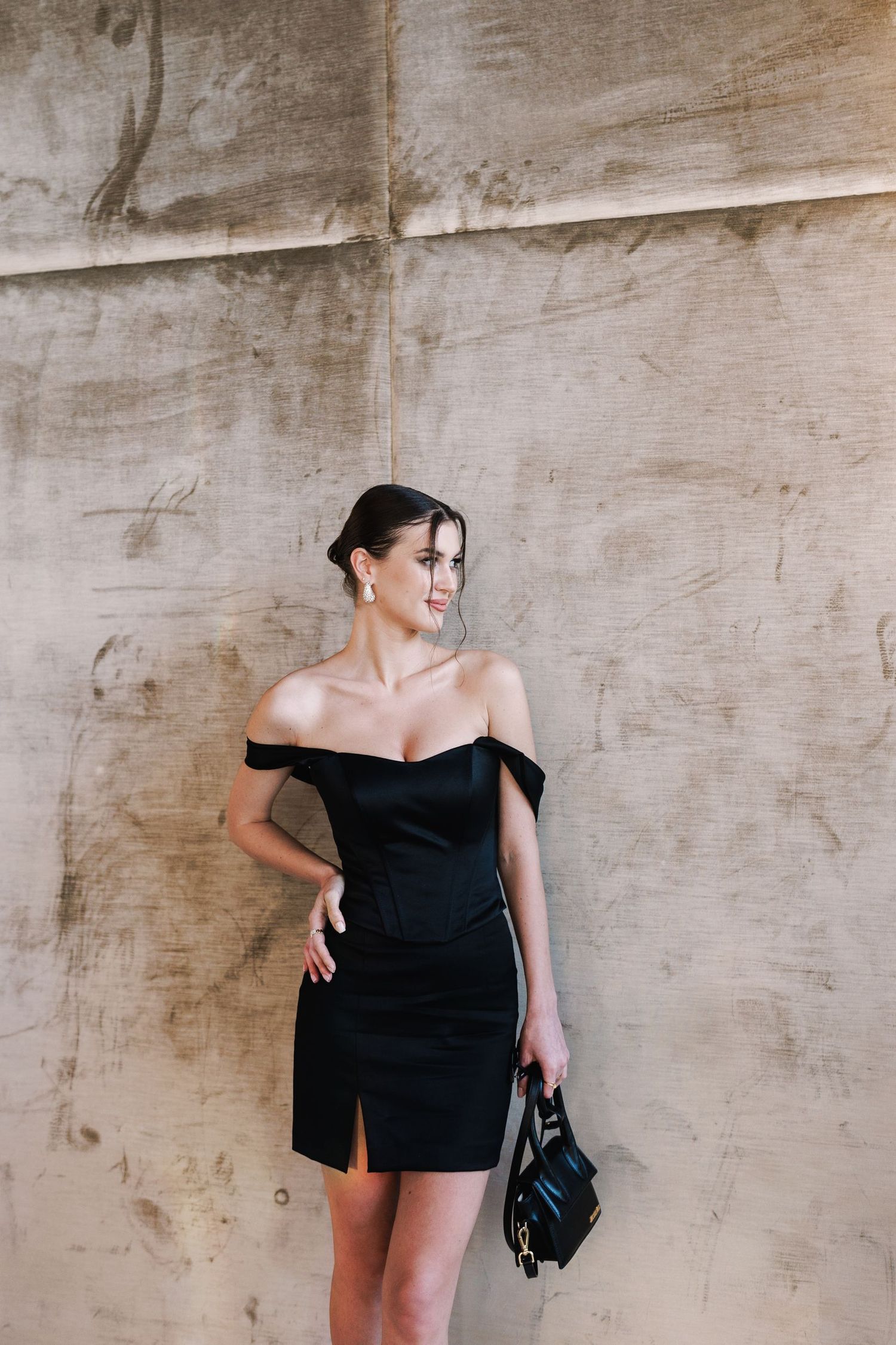 A stylish black mini dress photographed against a textured concrete wall.