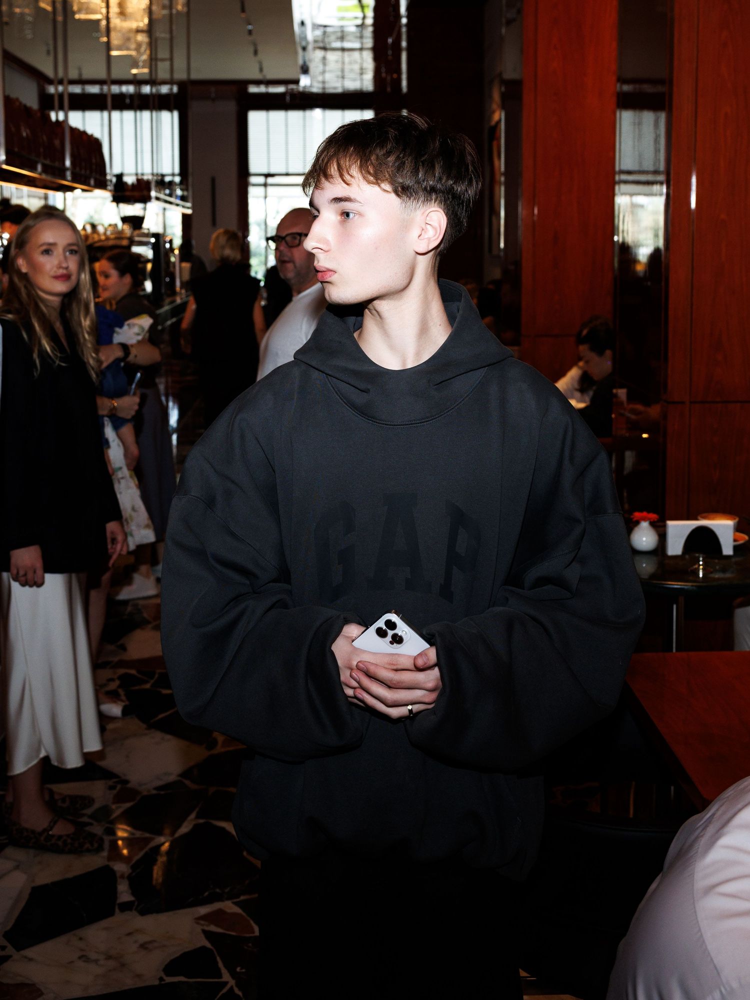 Person in black hoodie standing in dimly lit indoor space.