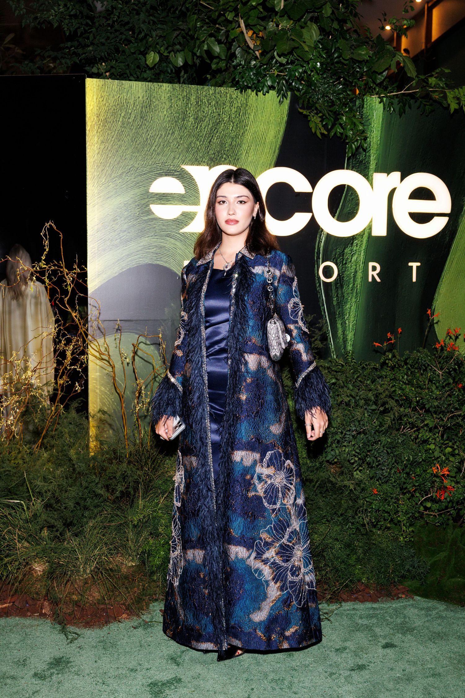 A fashion model wears a flowing navy blue tie-dye dress with ruffled details against a garden backdrop.
