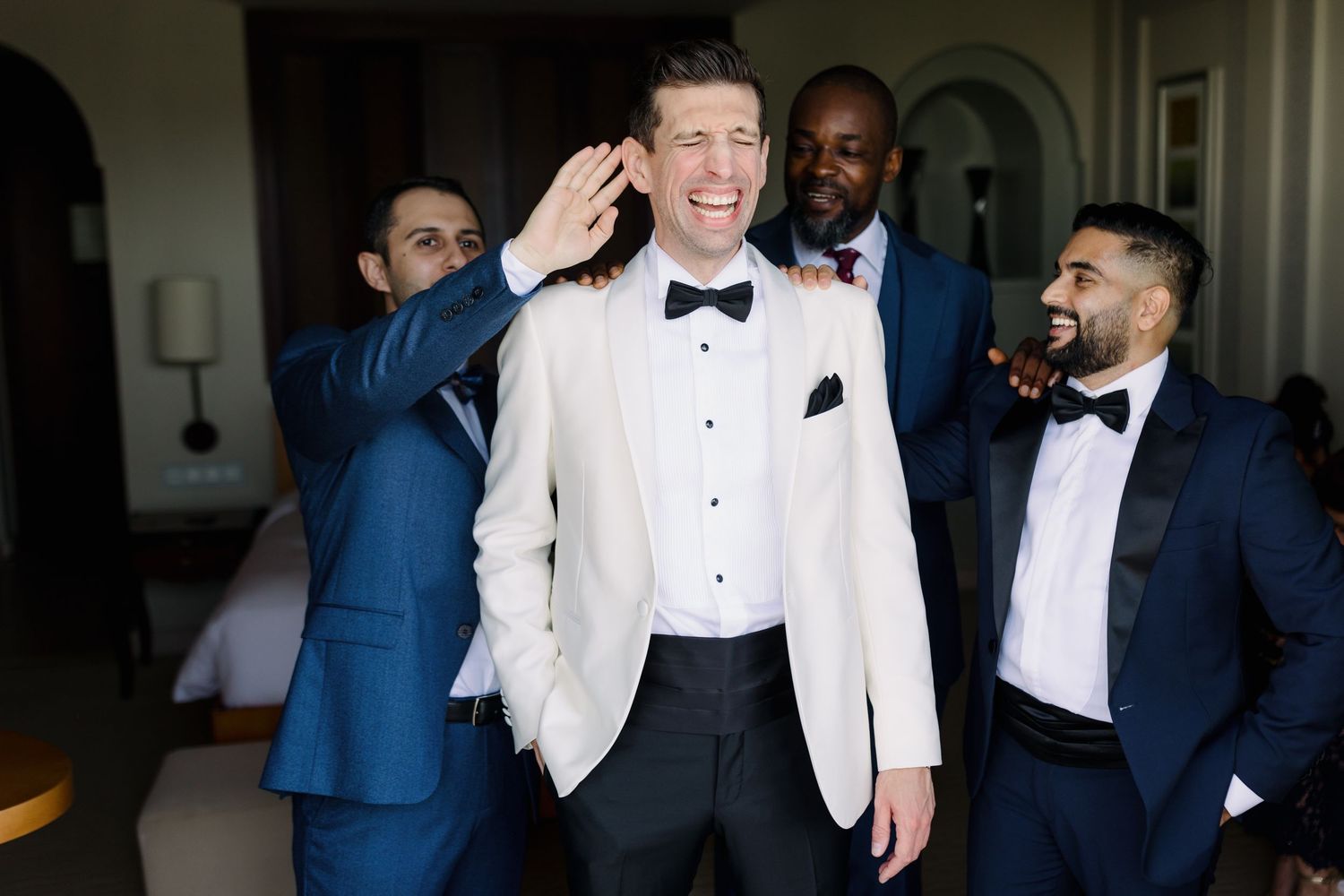 Wedding party members in formal attire share a fun candid moment indoors.