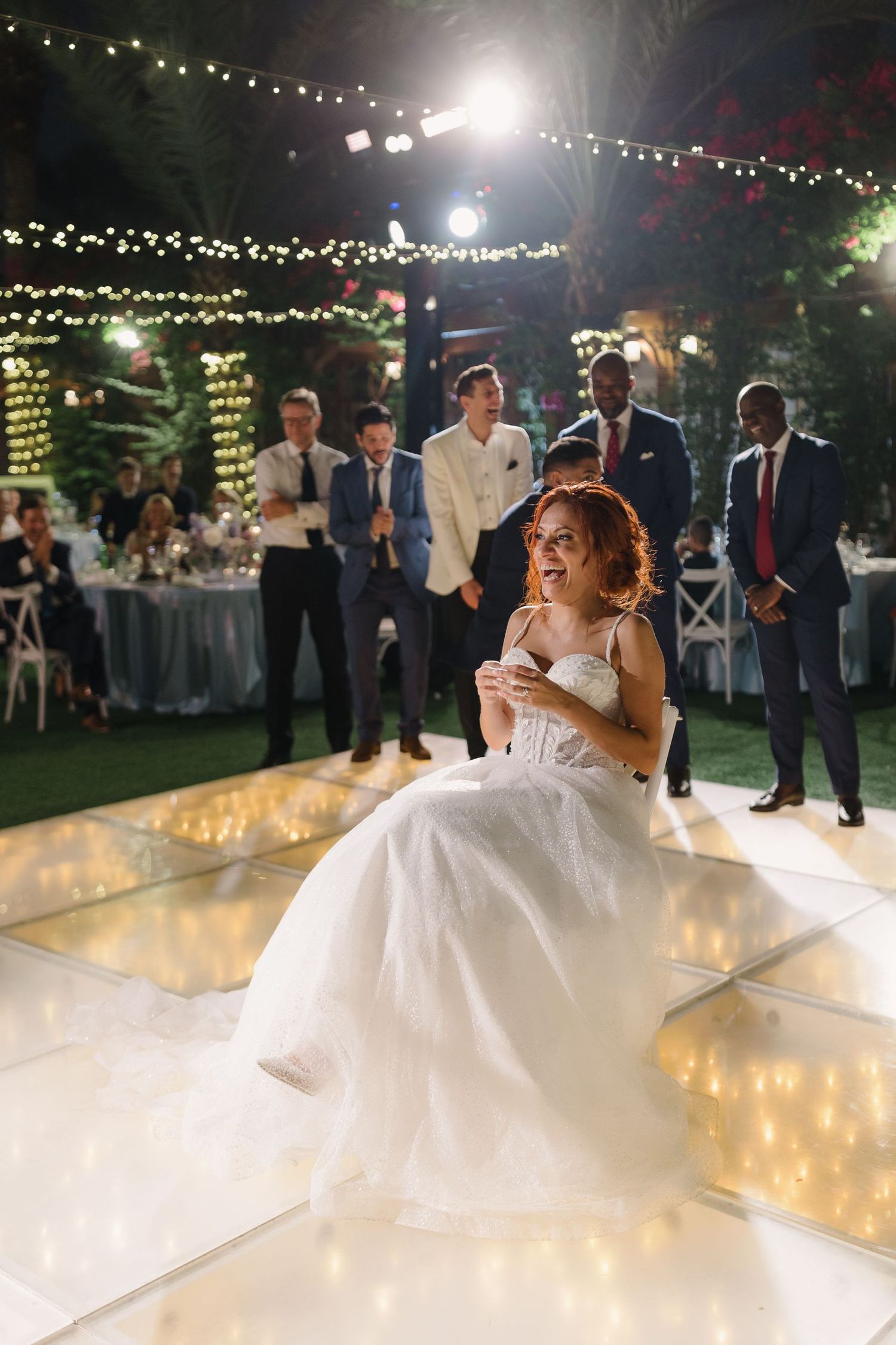 Couple shares their first dance on an illuminated dance floor under twinkling lights at an outdoor reception.