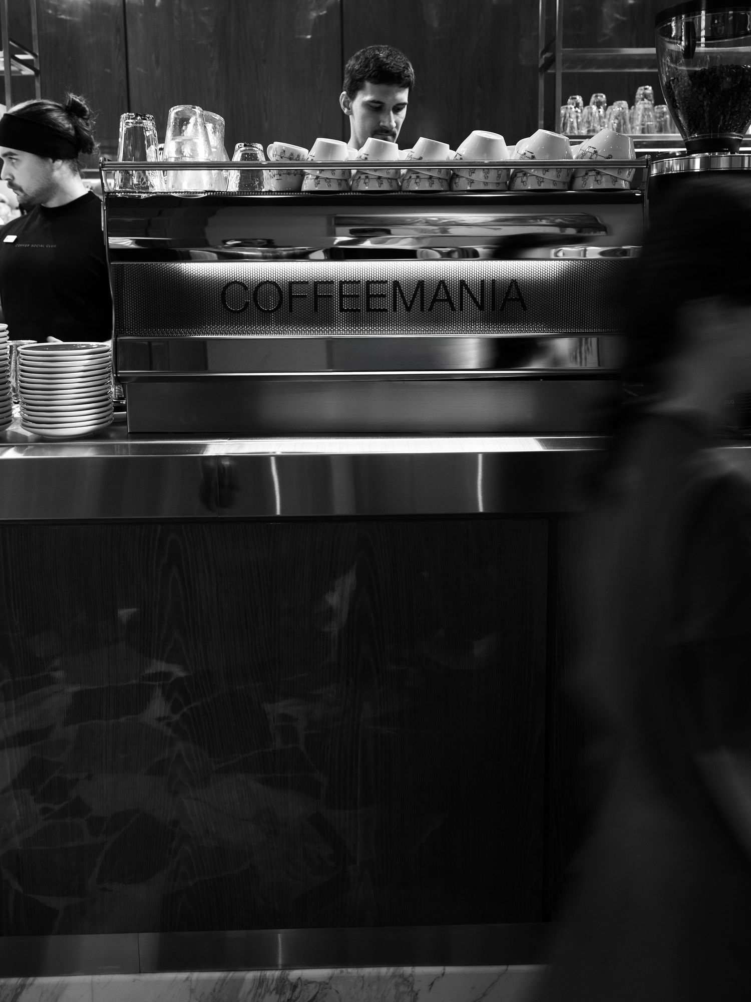 Interior view of a modern coffee shop counter with stacked cups and equipment in black and white.
