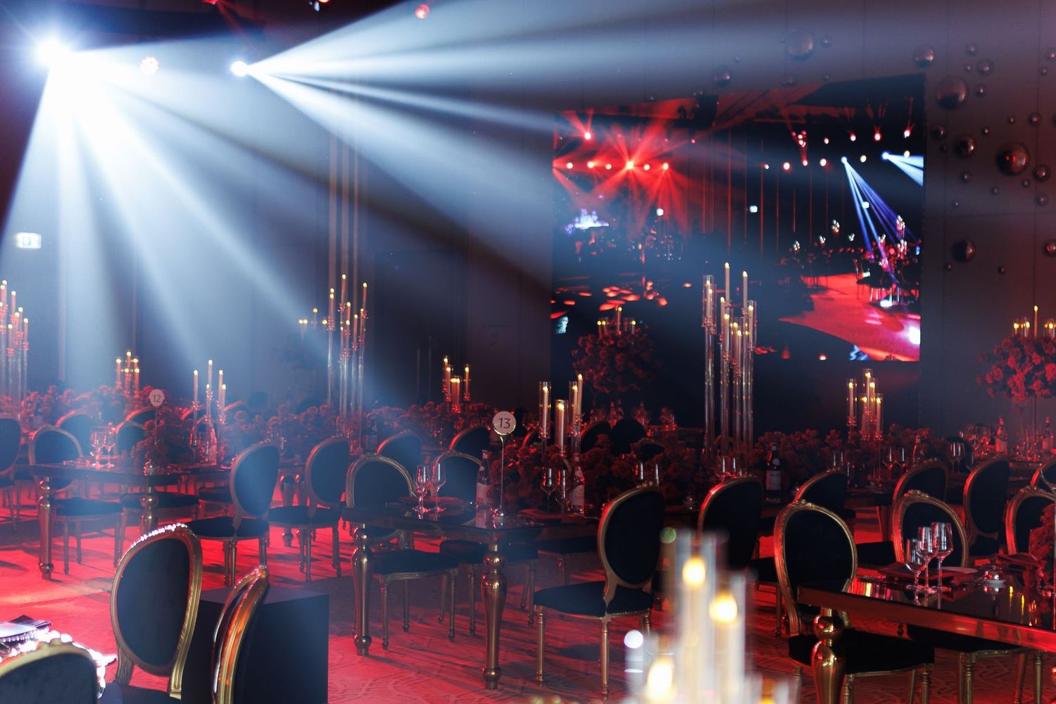 Concert or event space with dramatic white spotlight beams cutting through red ambient lighting.