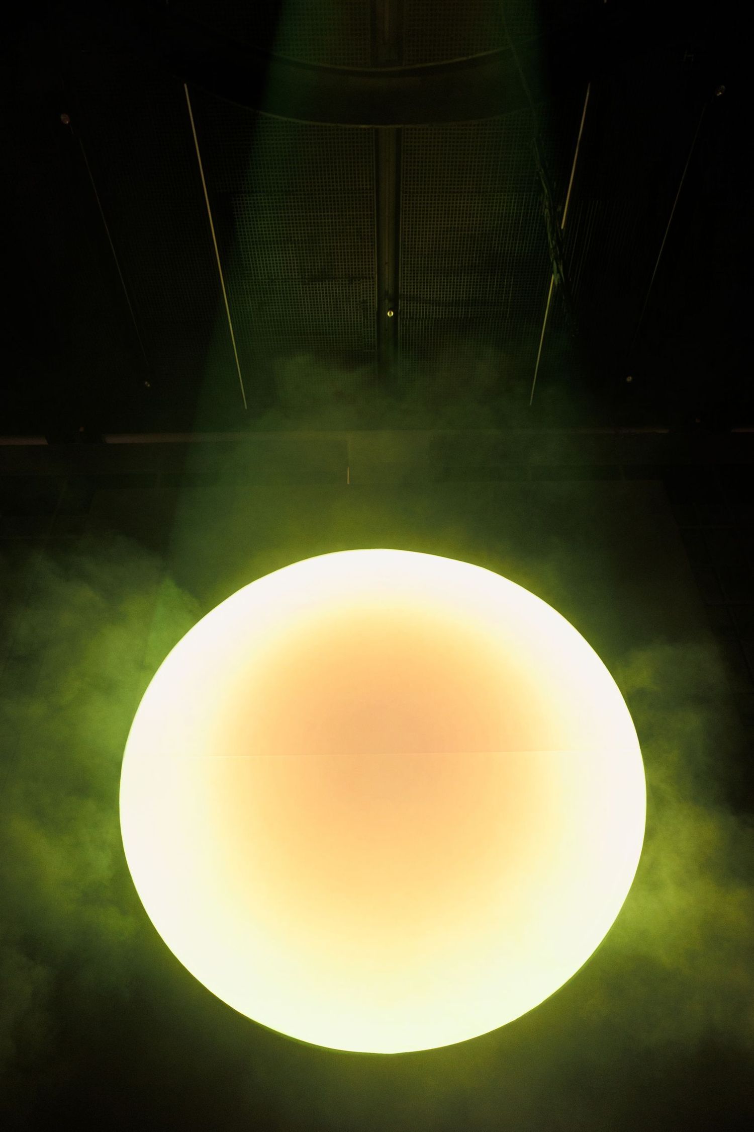 Glowing oval light fixture emitting green-tinted illumination in dark space.