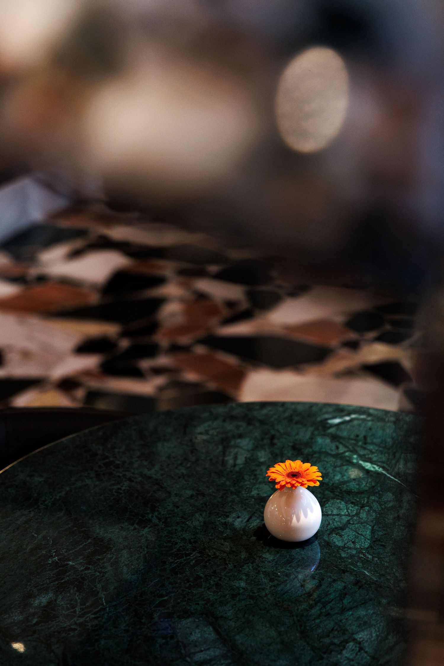 Minimalist table setting with orange flower and white ceramic piece on dark surface.