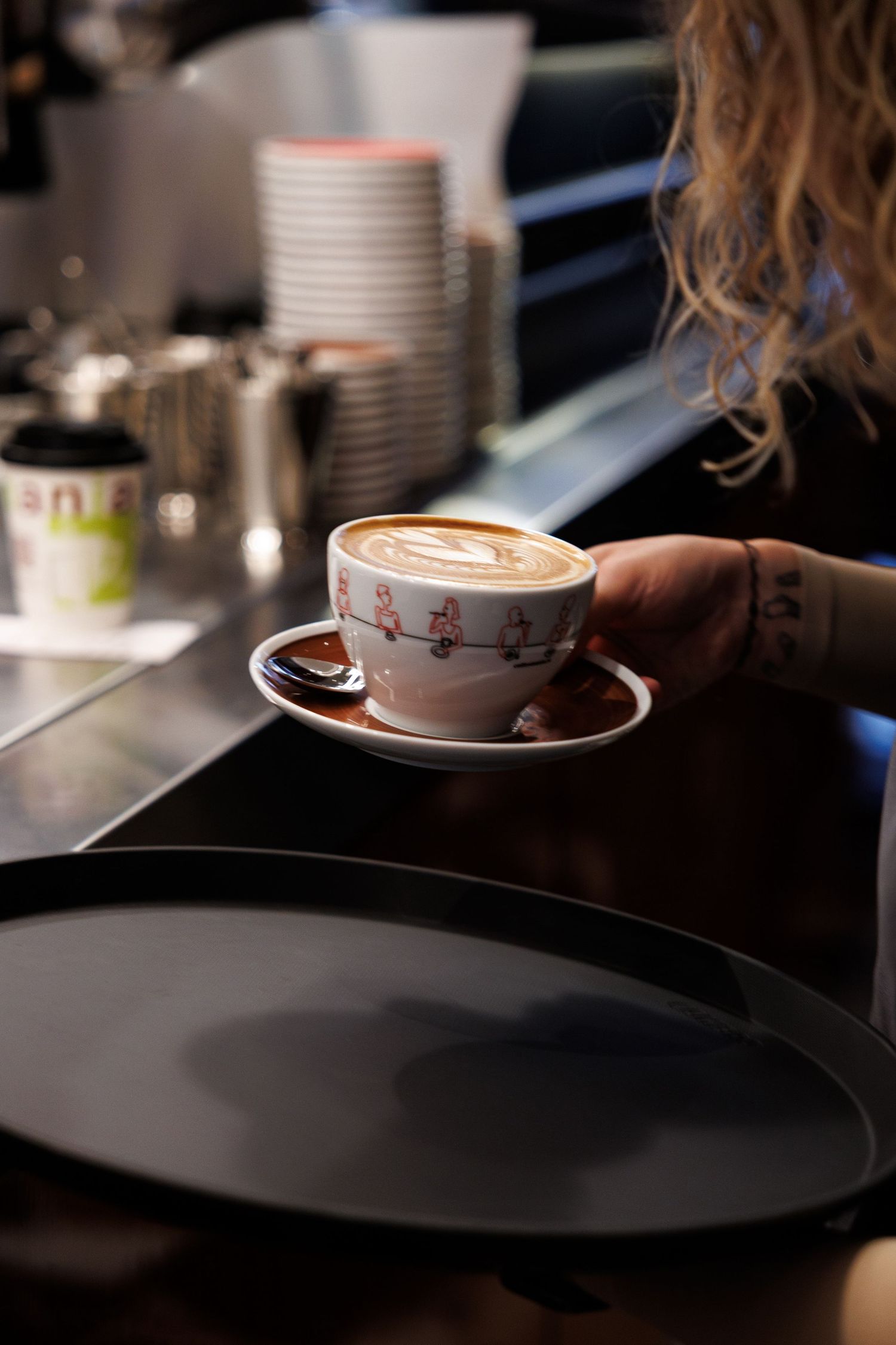 A latte with decorative foam art being served in a patterned coffee cup on a dark surface.