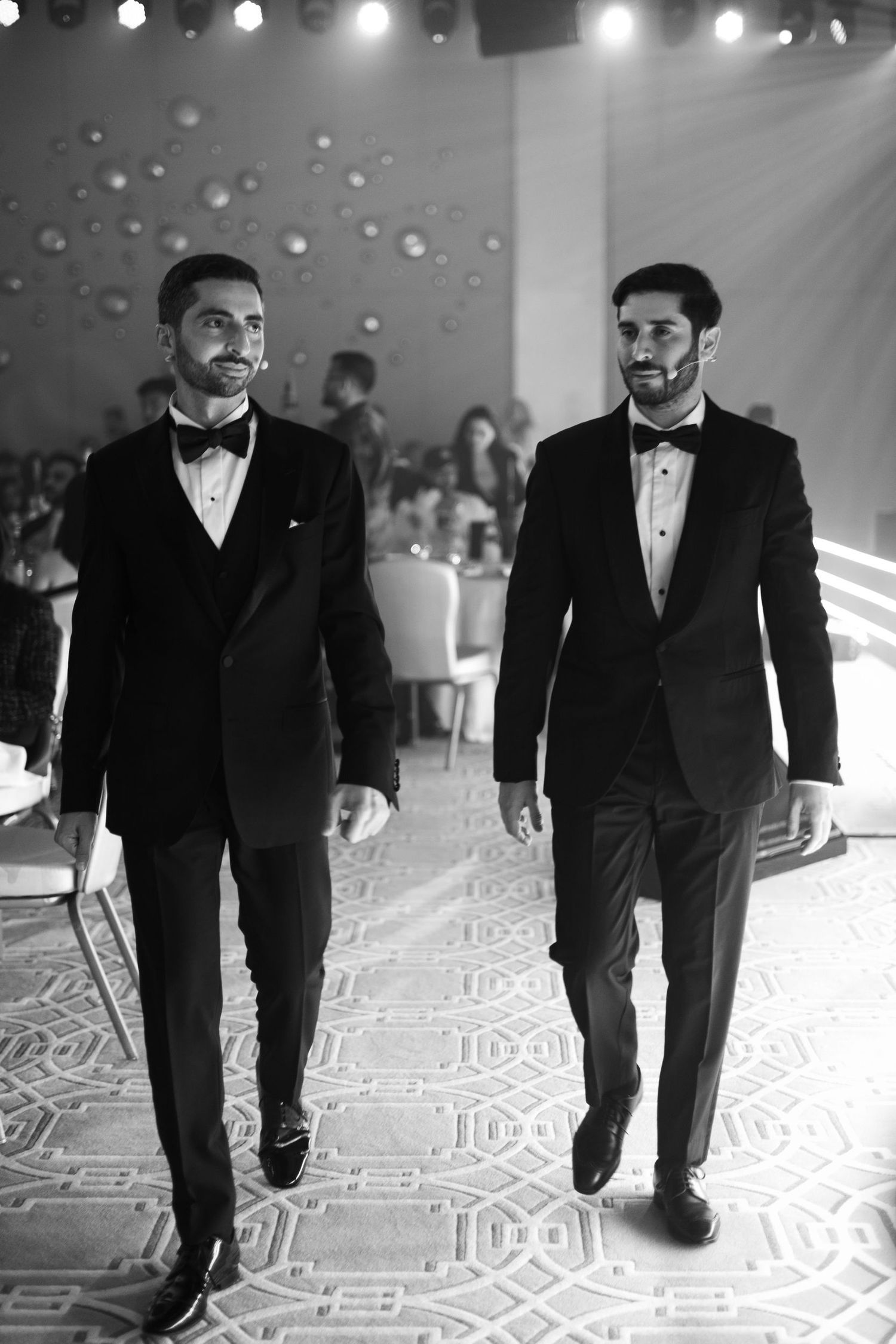 Group walking across patterned floor at formal black-tie event.