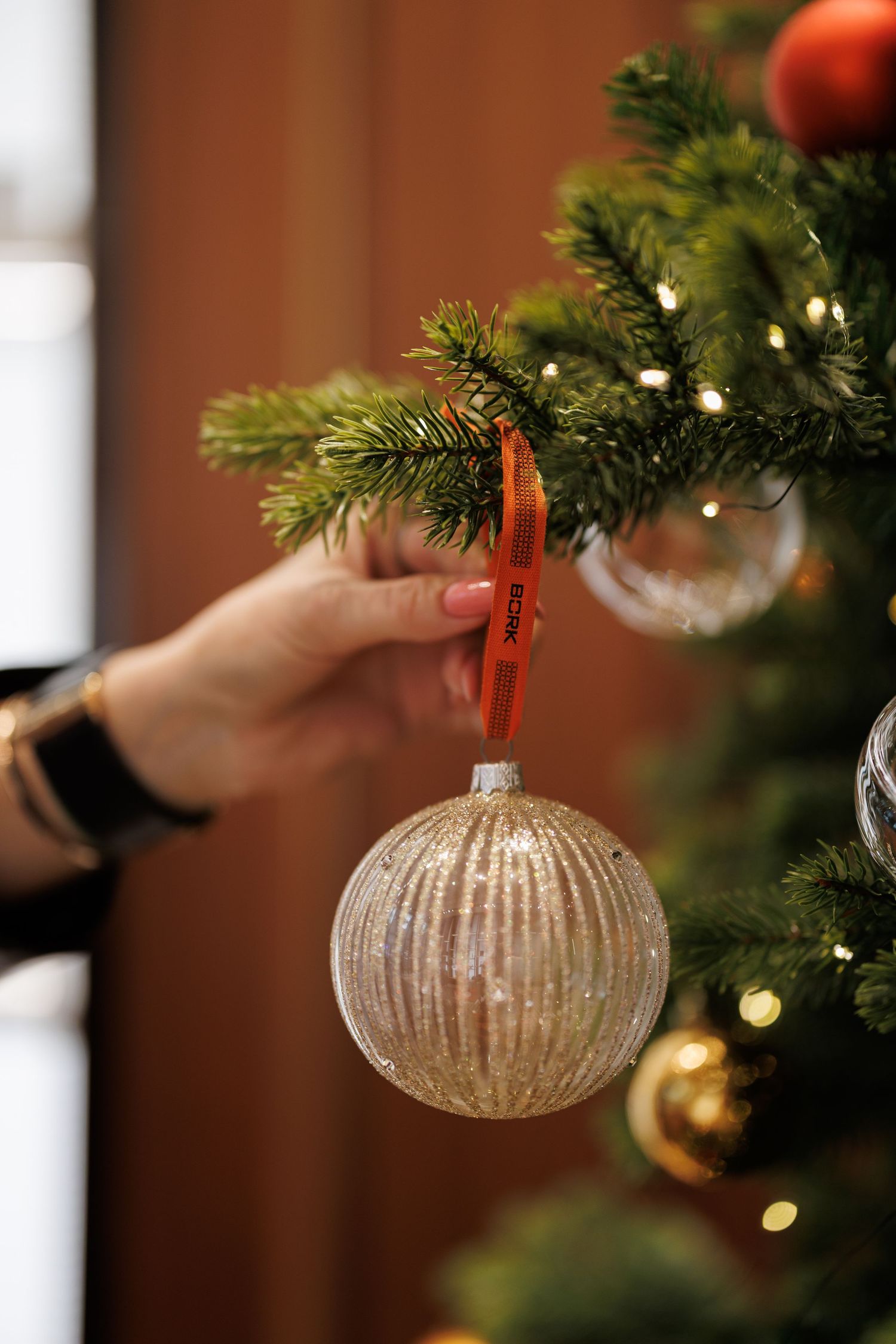 Close-up of silver glass ornament hanging on Christmas tree branch with warm lighting.