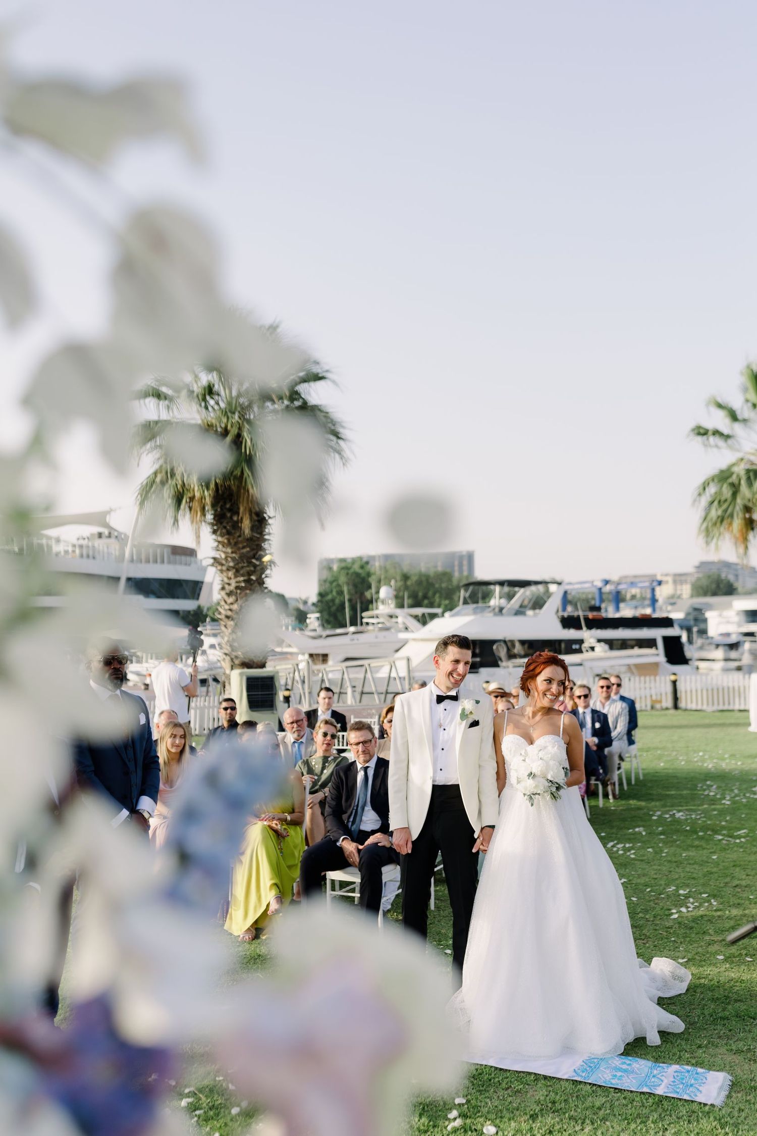 Wedding guests gathered on a grassy lawn with palm trees and decorations.