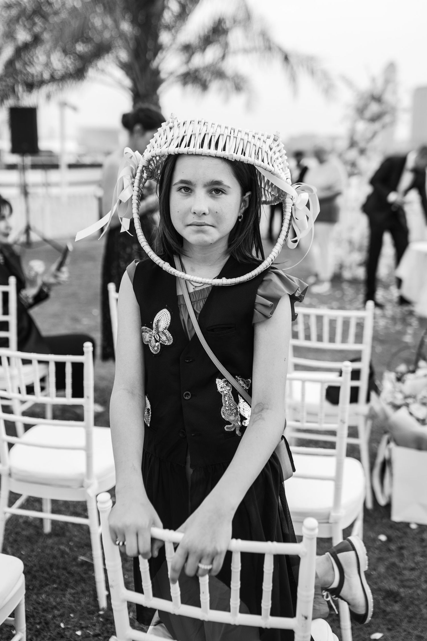 Guest in black dress with unique circular headpiece at outdoor wedding.