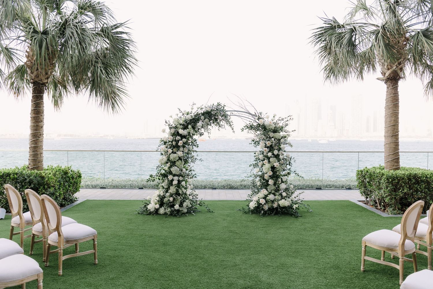 Outdoor wedding ceremony setup with white chairs and palm trees overlooking the water.
