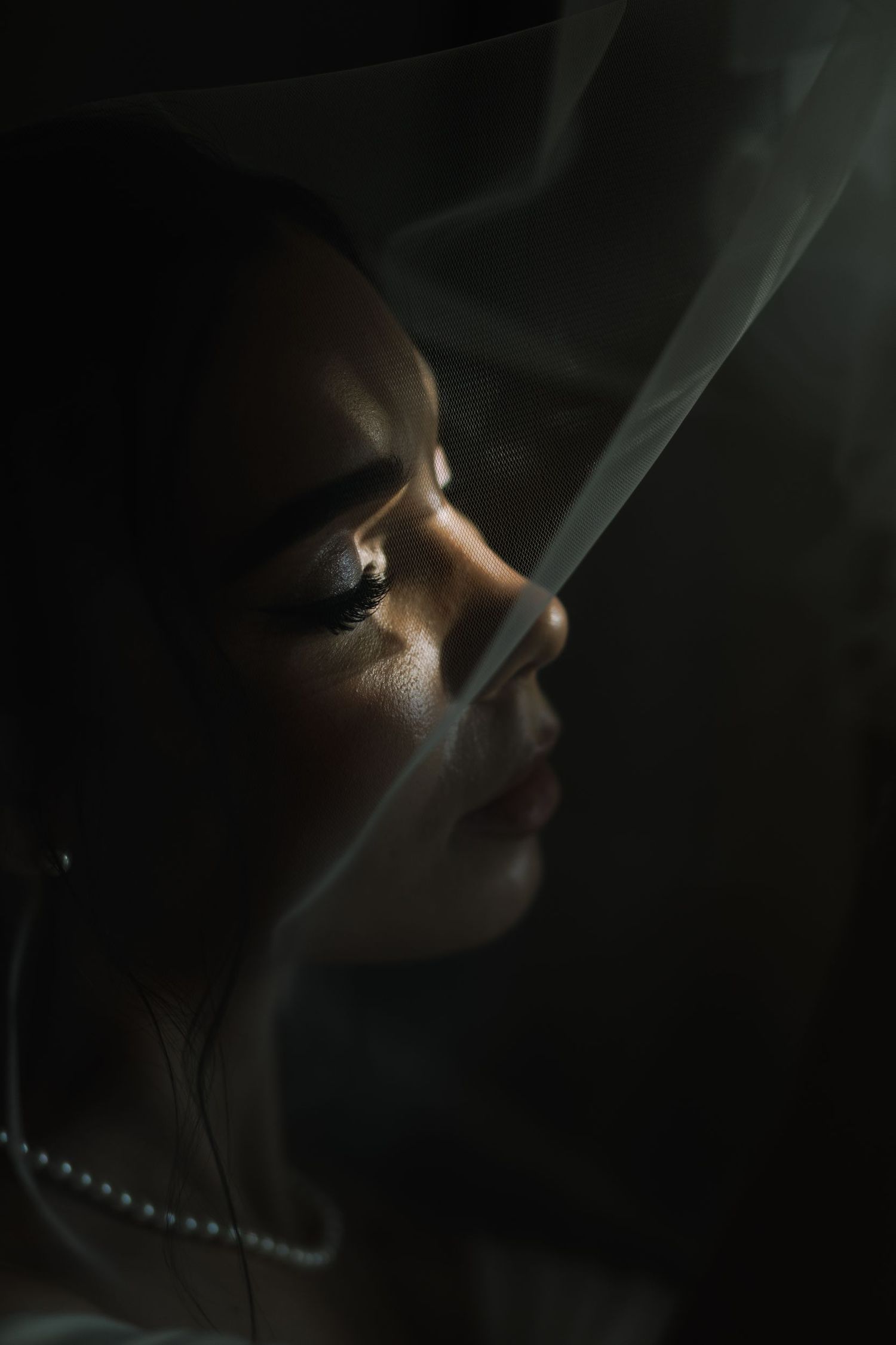 Moody low-light portrait with dramatic shadows and pearl necklace detail.