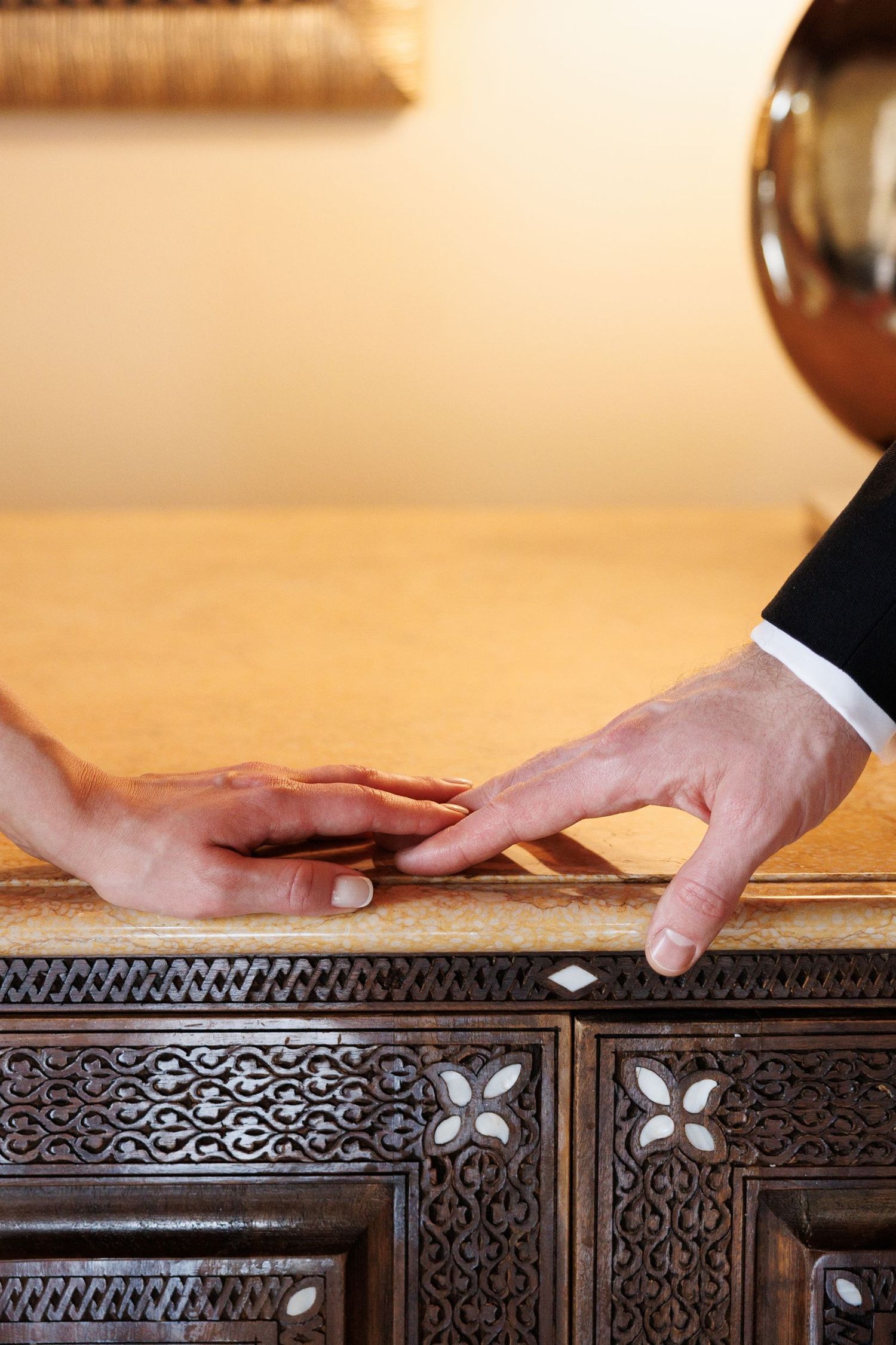 Close-up details of hands touching an ornately carved wooden dresser or cabinet.