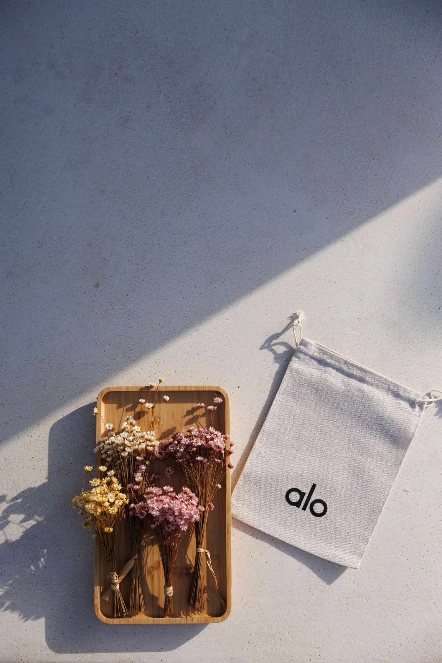 Minimalist flat lay of dried flowers in a wooden tray with 'alo' branding on white surface.