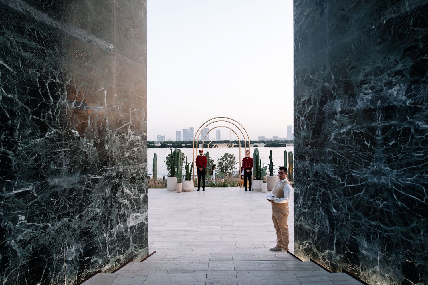 A panoramic view of people walking through a dark marble corridor leading to a bright outdoor space.