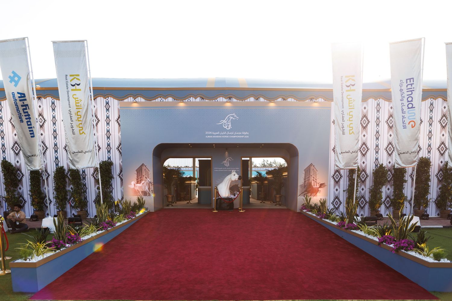 A red carpet entrance walkway with white pillars and decorative lighting leads to an elegant archway entrance.