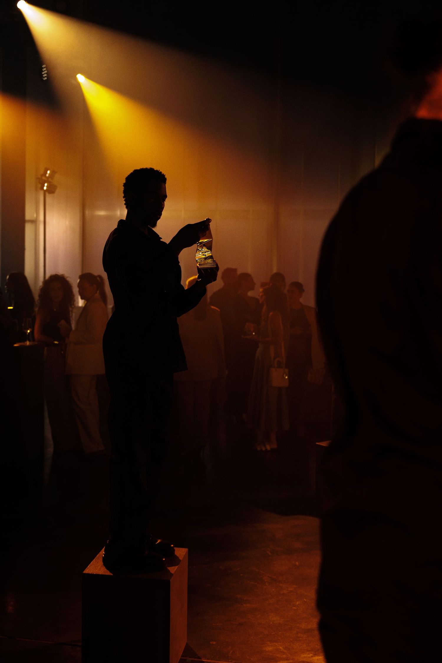 Silhouettes of people moving through a dimly lit space with dramatic yellow lighting.