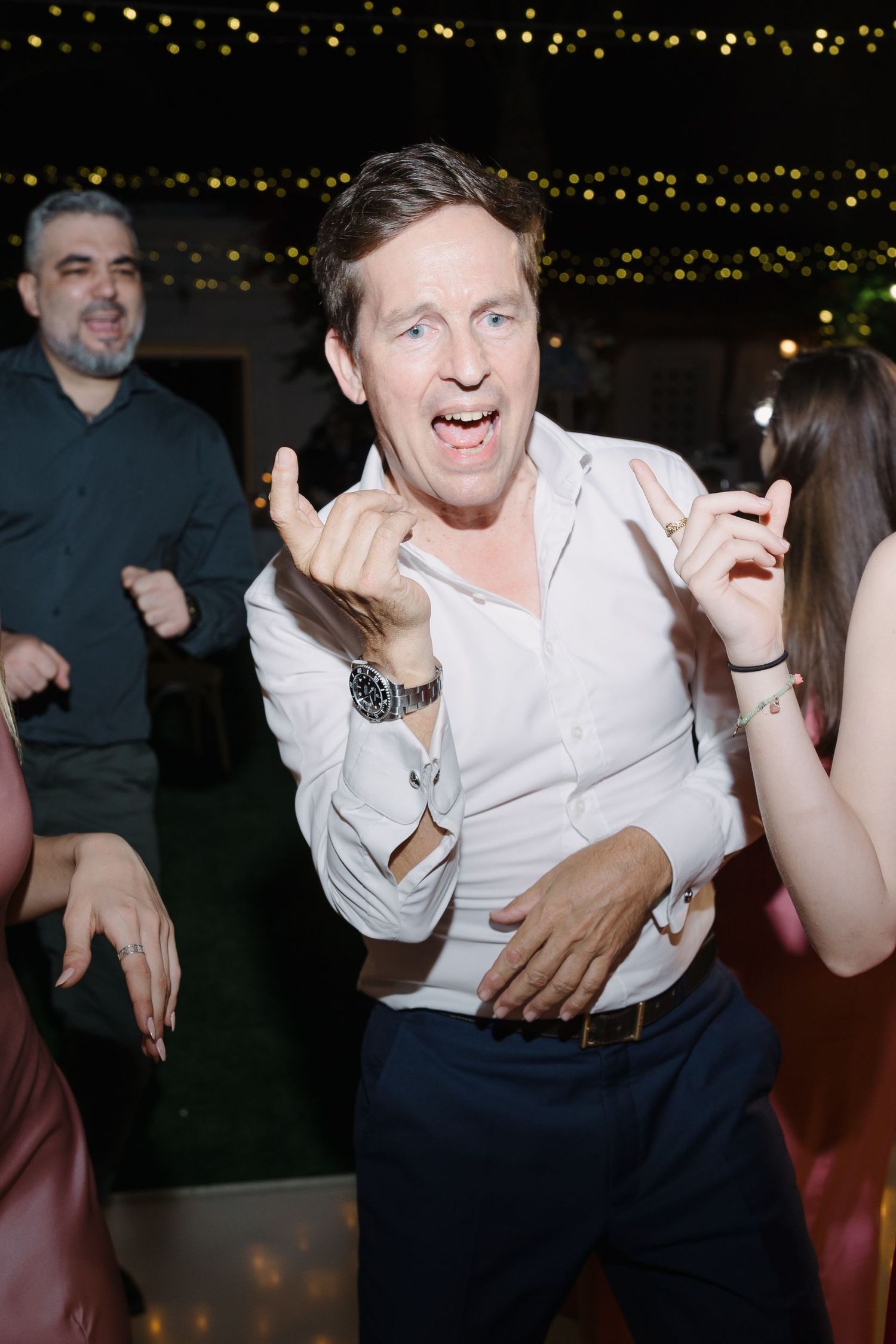 Wedding guests dancing energetically and joyfully at a reception with twinkling lights in the background.